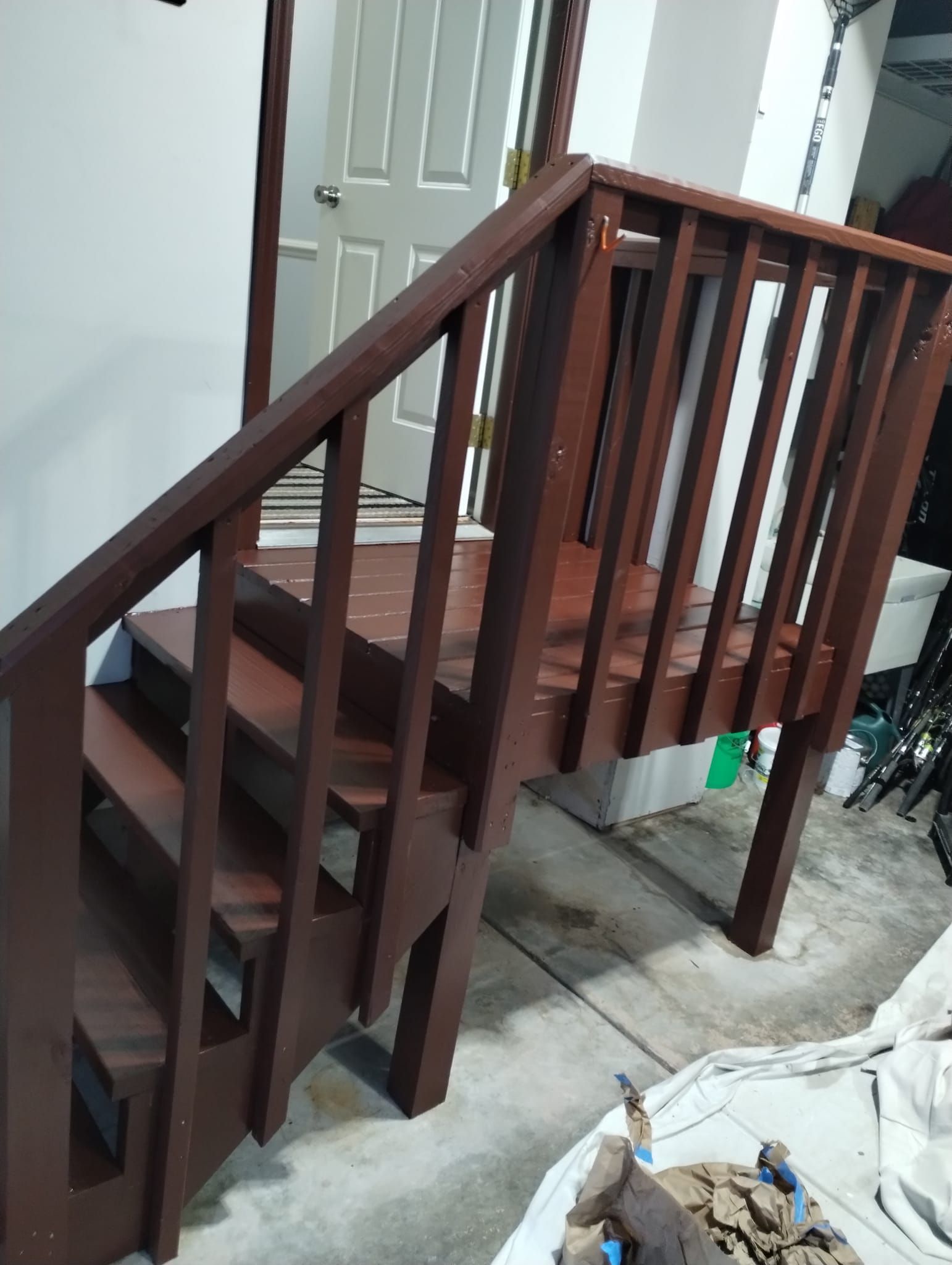 Wooden staircase painted brown leading to a door, with a railing on one side.