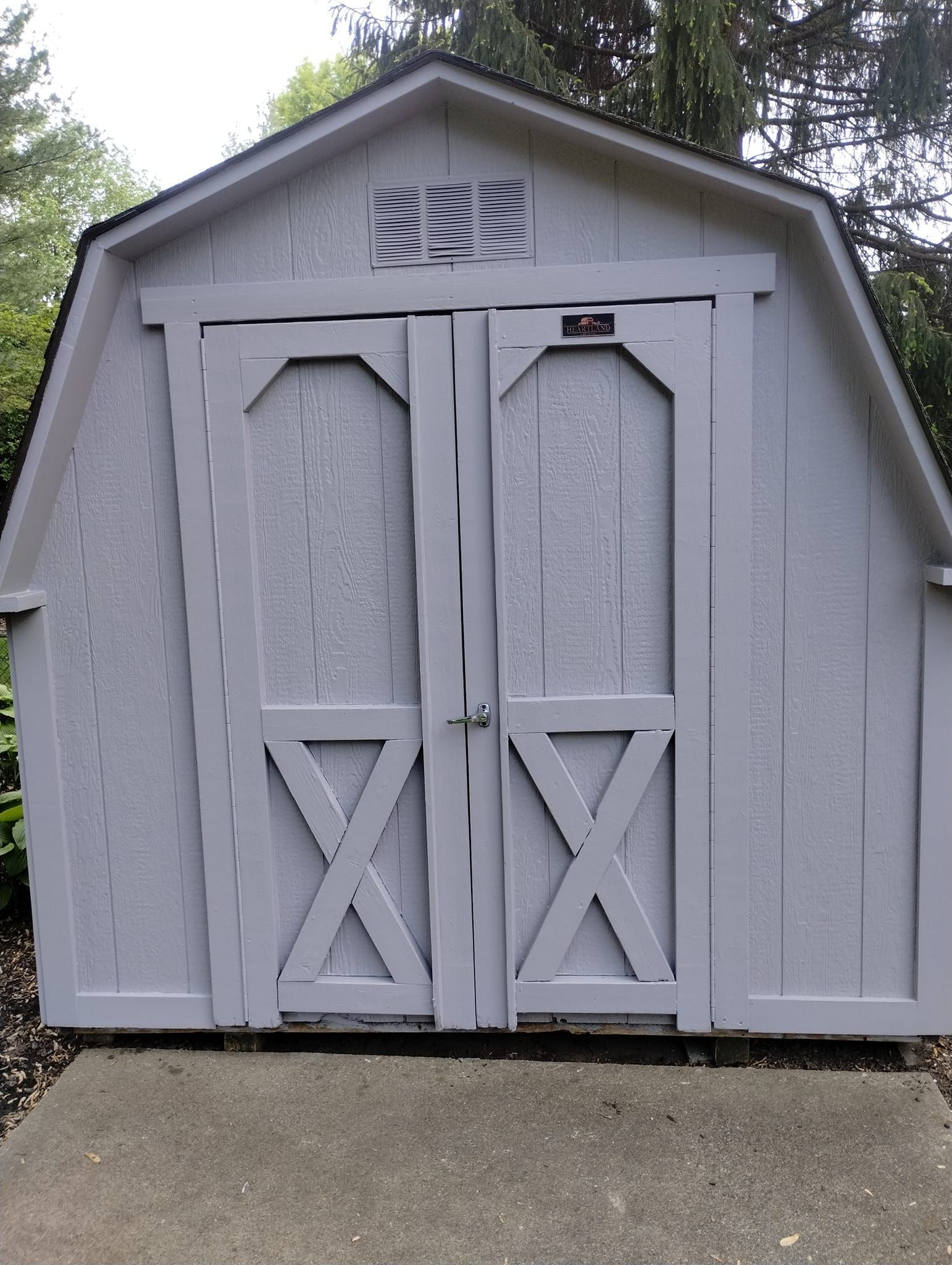 Gray wooden shed with double doors and an X design.