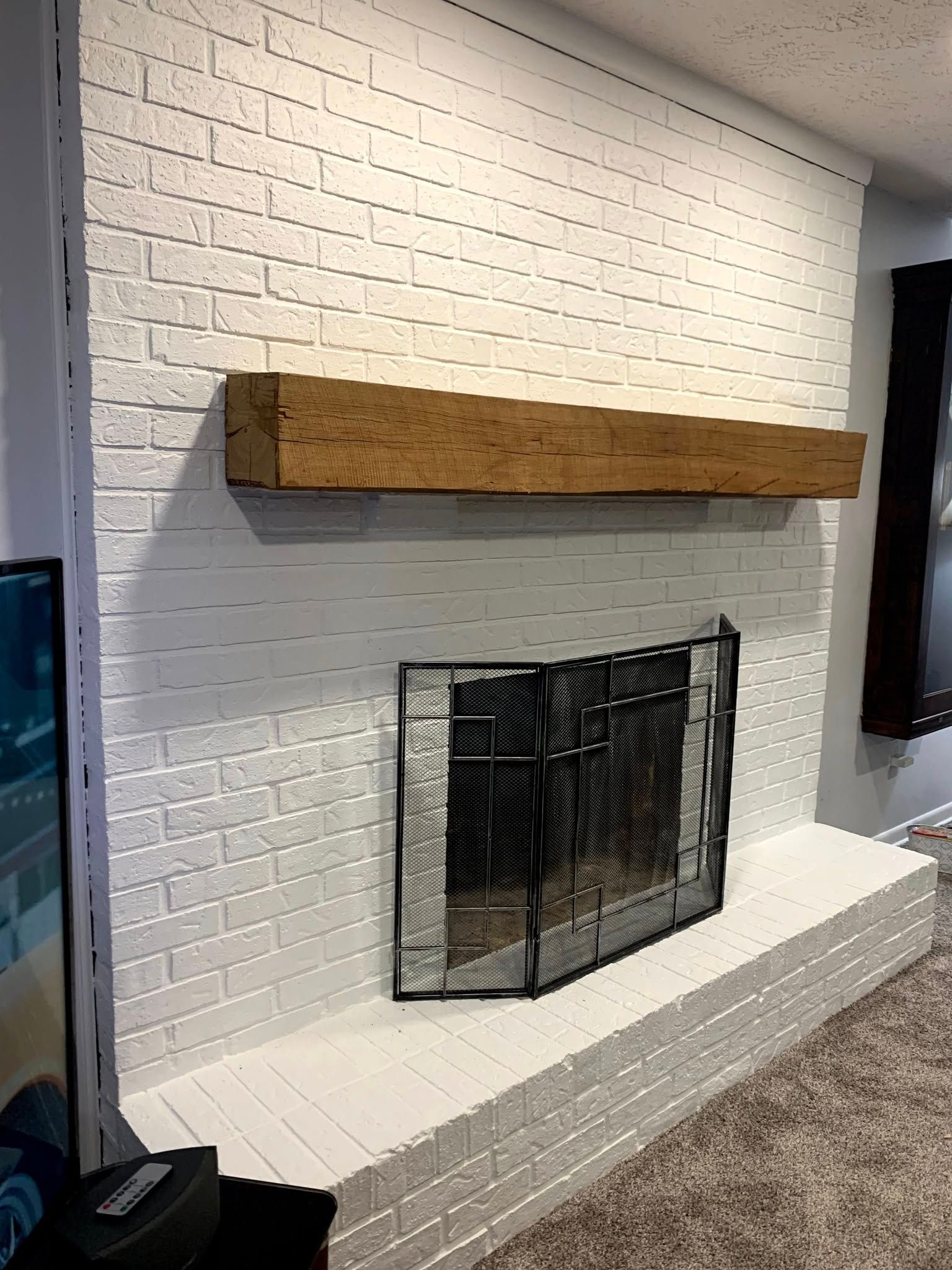 White brick fireplace with a wooden mantel and black fire screen.