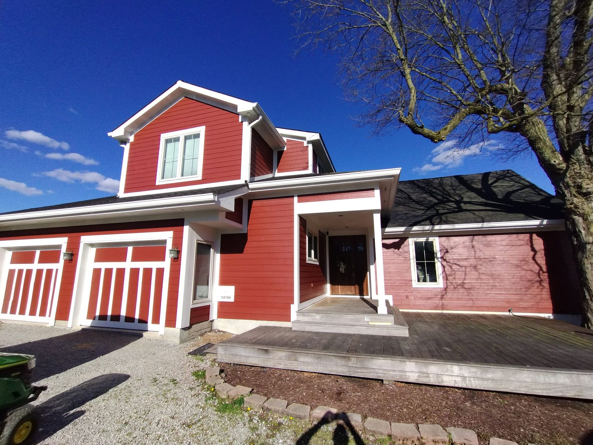 Red house with three-car garage, front porch, and black roof under a bright blue sky.