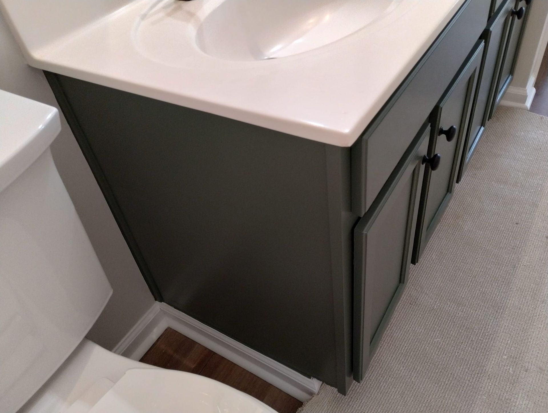 Bathroom vanity with a white countertop and dark green cabinets next to a toilet.