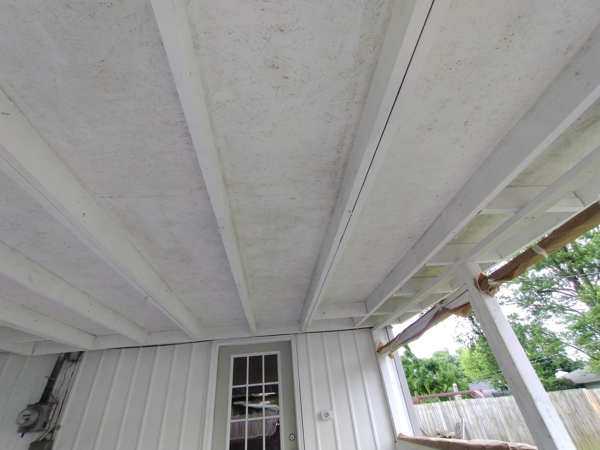 White painted porch ceiling with supporting beams. Door and exterior wall in view.