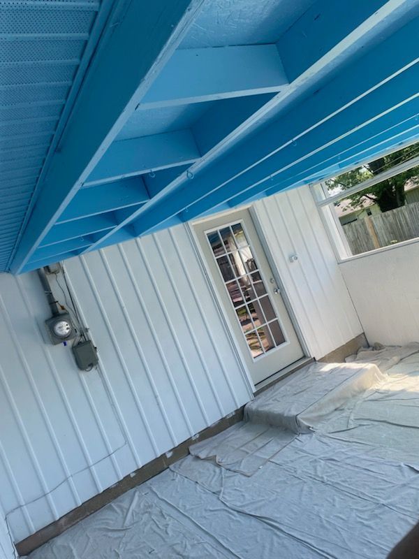 Blue-painted porch ceiling with white siding, door, and ground cover. Electrical meter visible.