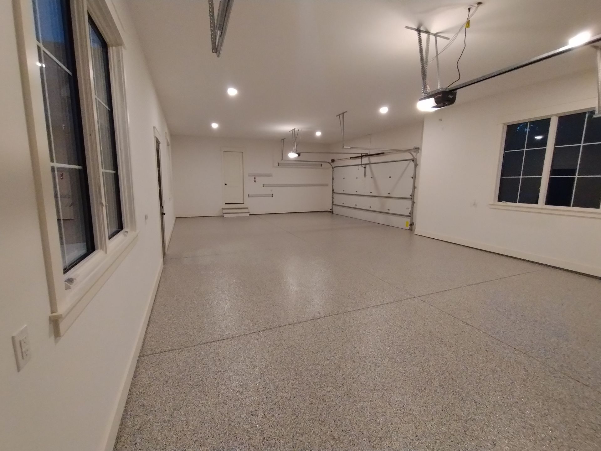Empty garage with epoxy floor, garage doors, windows, and white walls.