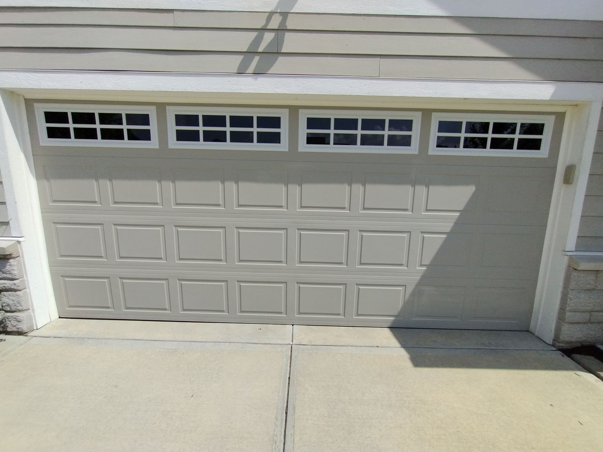 Garage door with windows, beige with white trim, on a concrete driveway.