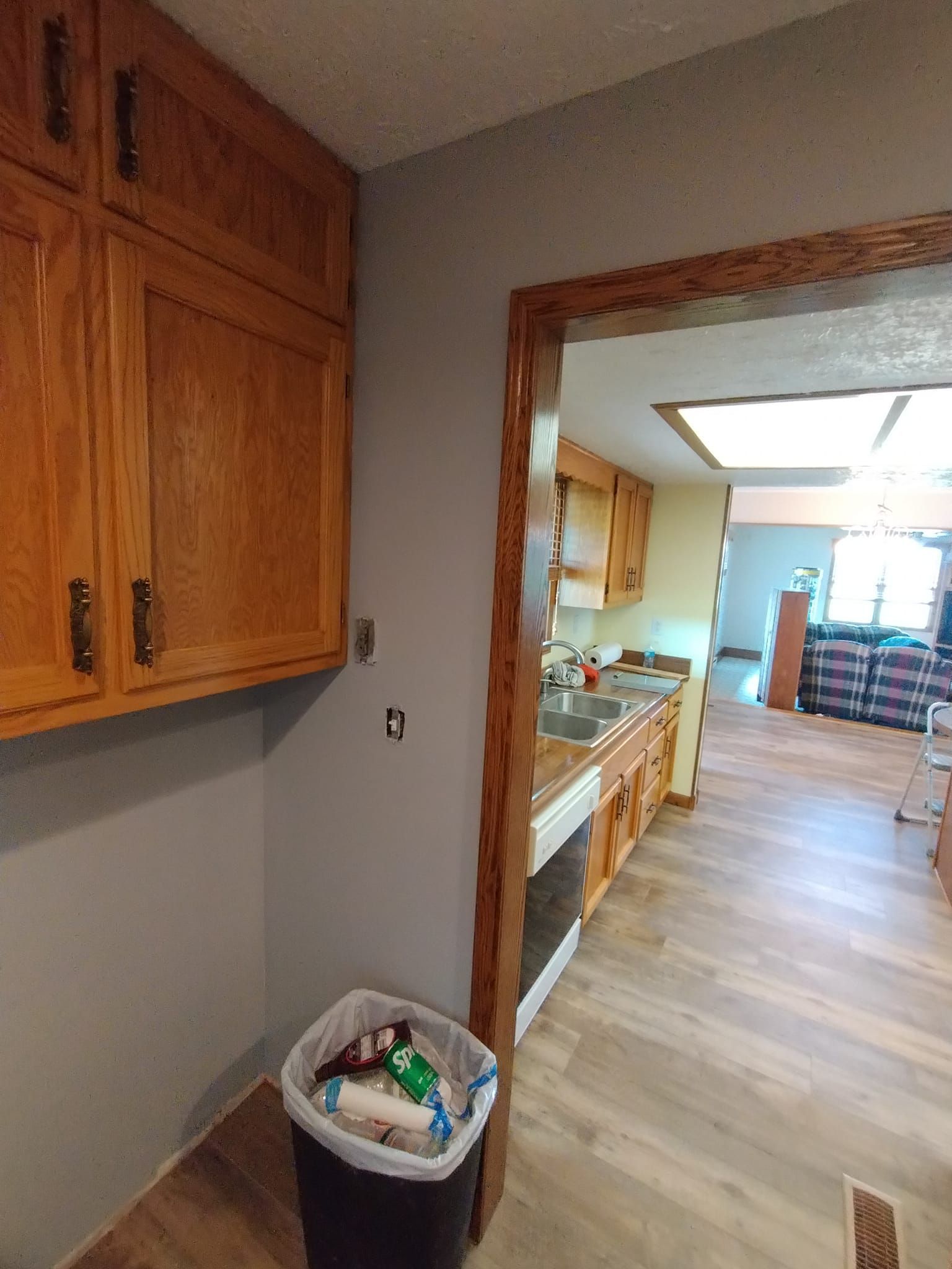 A kitchen with wooden cabinets and a trash can in the corner.