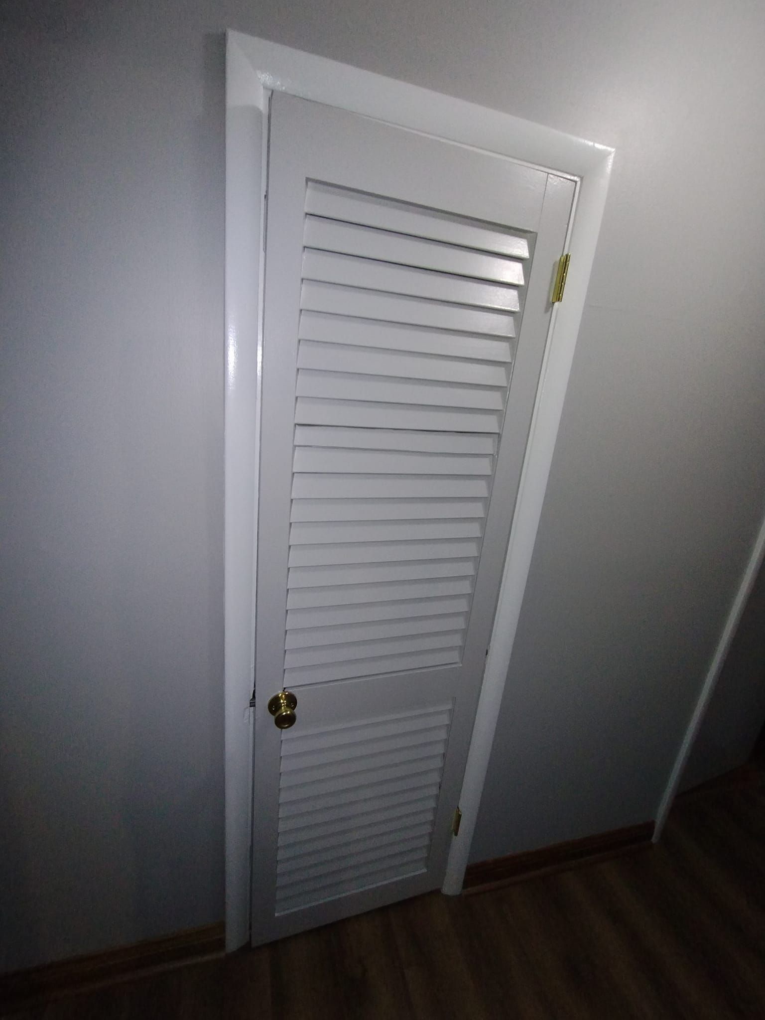 A white door with shutters on it is open in a dark room.