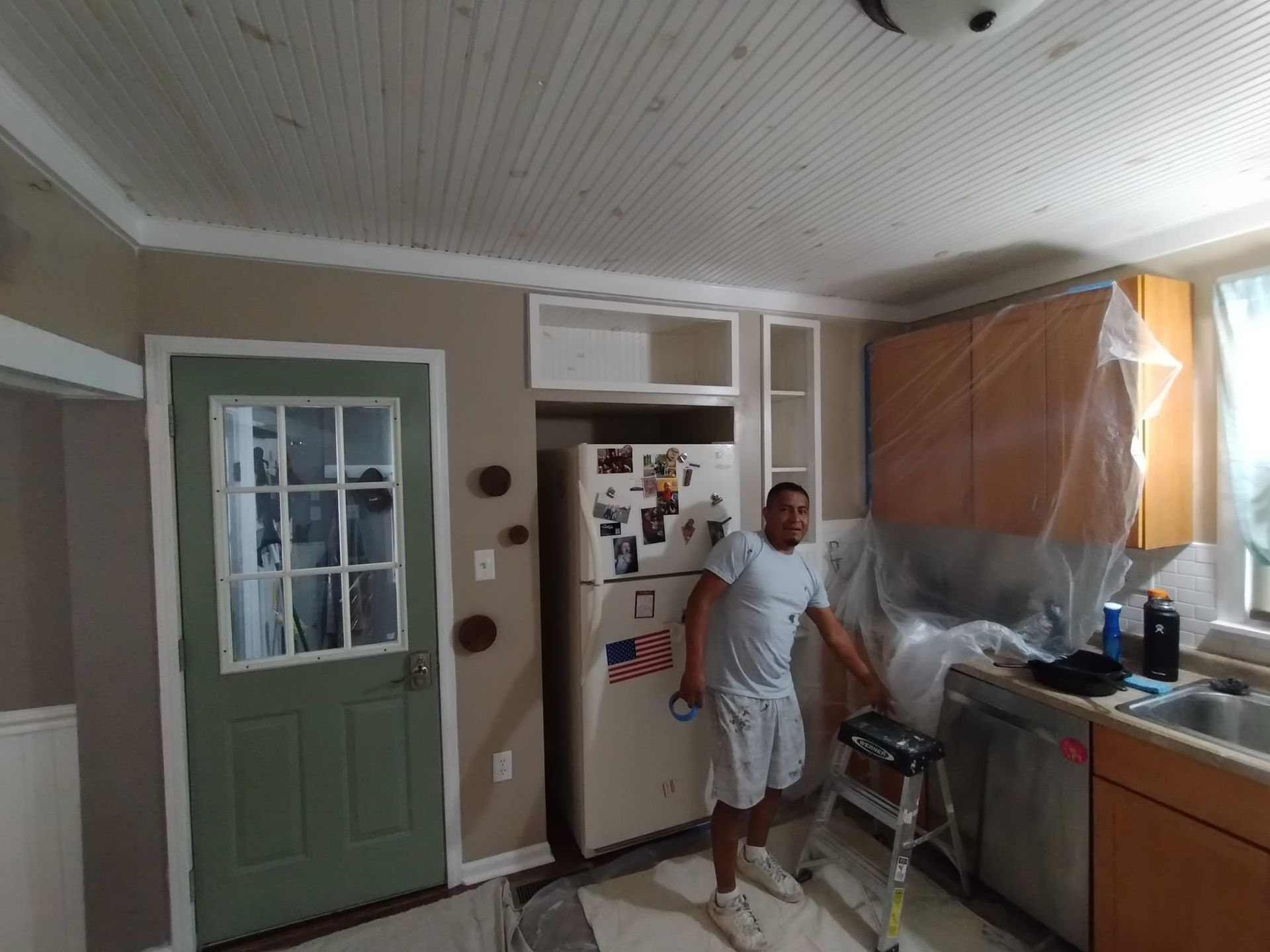 A man is standing in a kitchen covered in plastic.