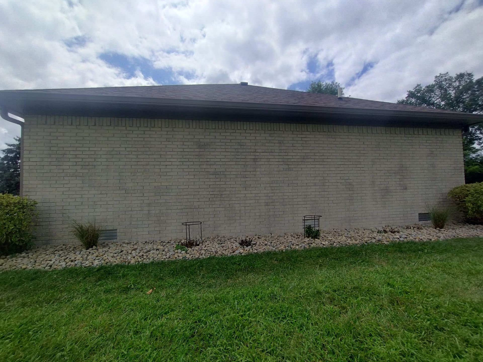 A white brick house with a roof is sitting on top of a lush green lawn.