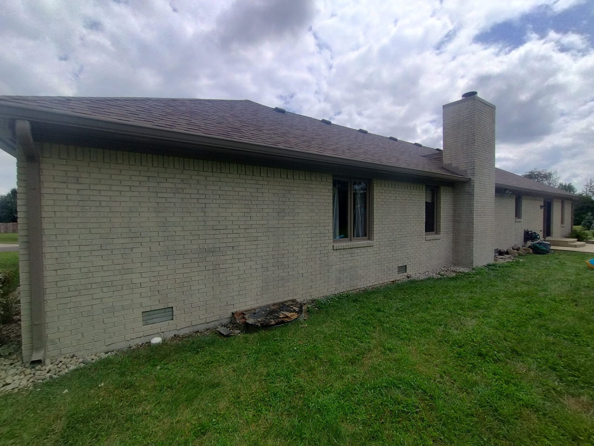 A white brick house with a brown roof is sitting on top of a lush green field.