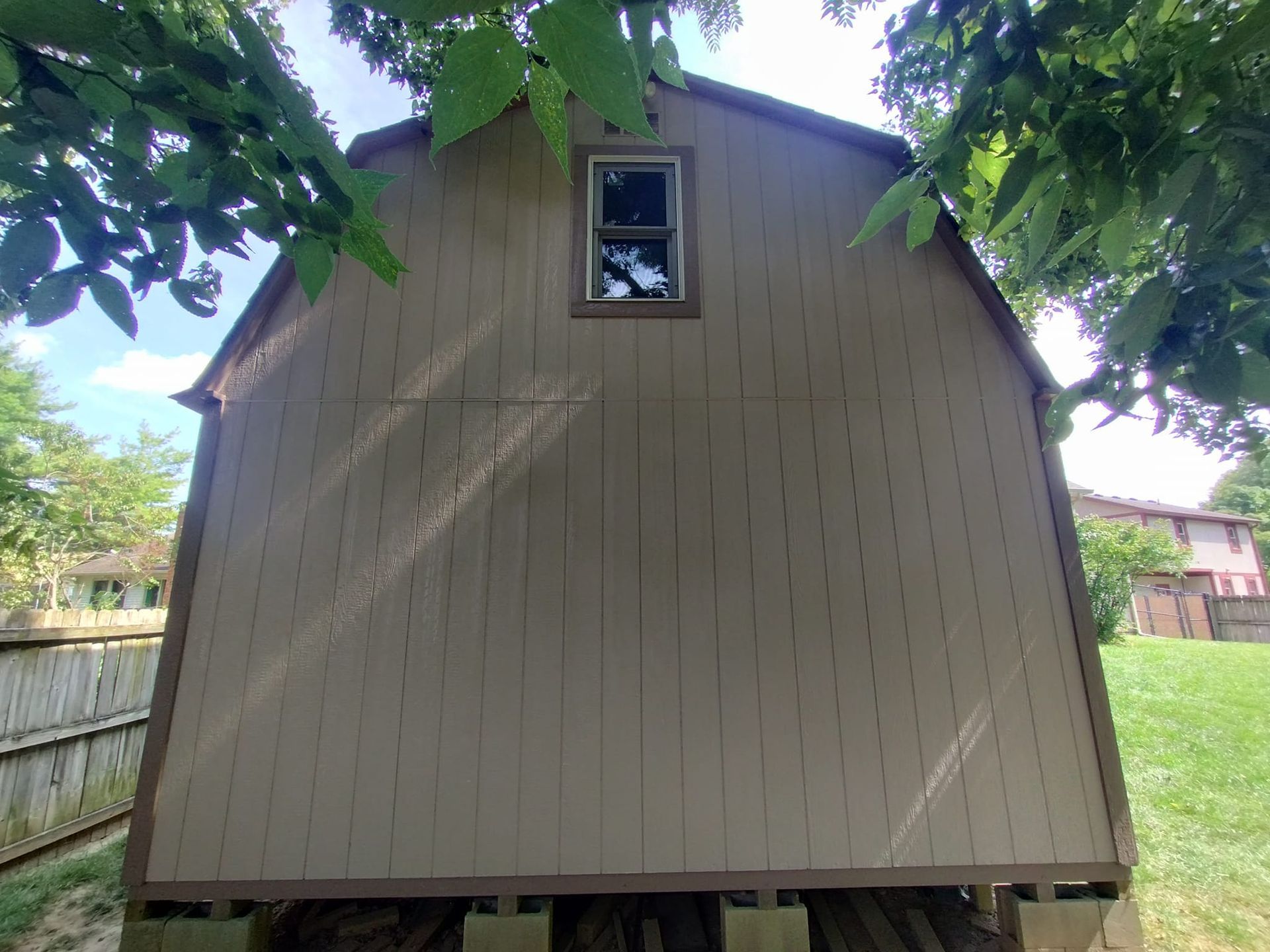 The back of a barn with a window and a fence in the background.