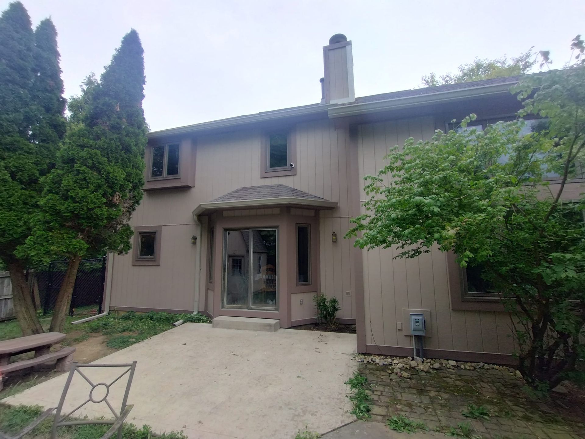 The back of a house with a patio and trees in front of it.