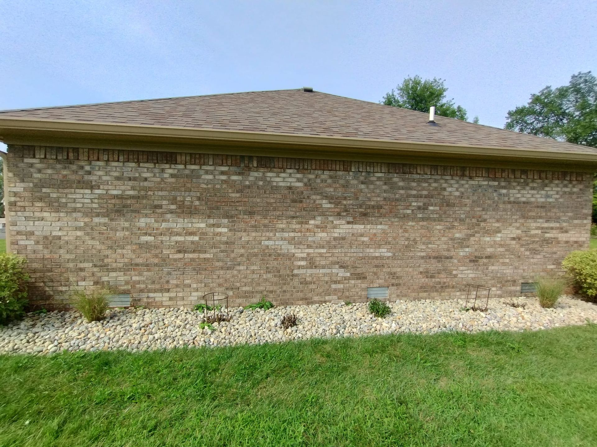 A brick building with a brown roof is sitting in the middle of a lush green field.