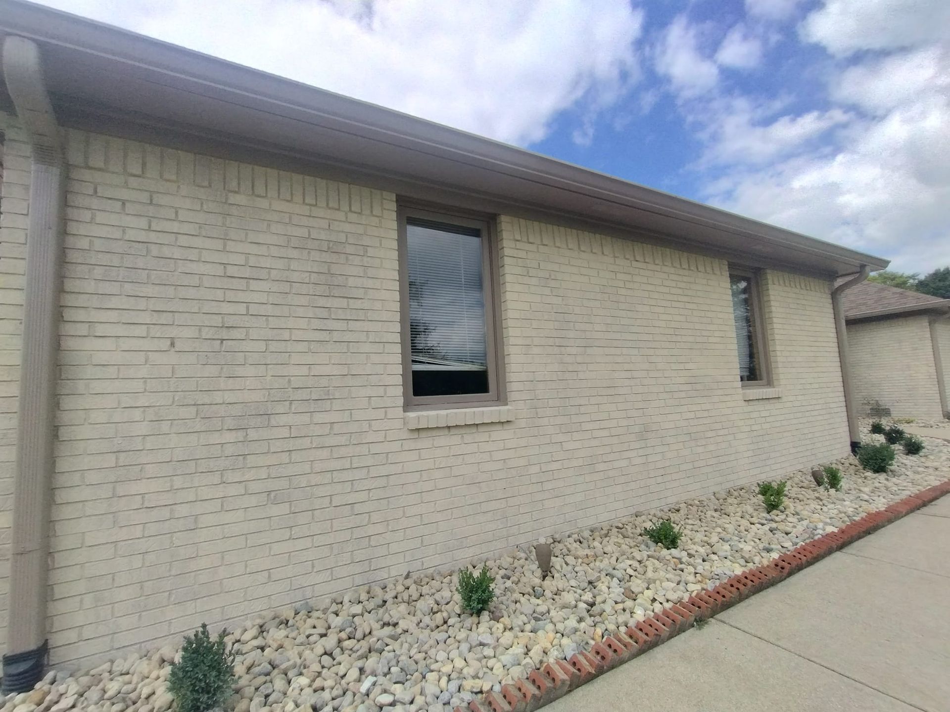A white brick house with two windows and a gutter on the side of it.
