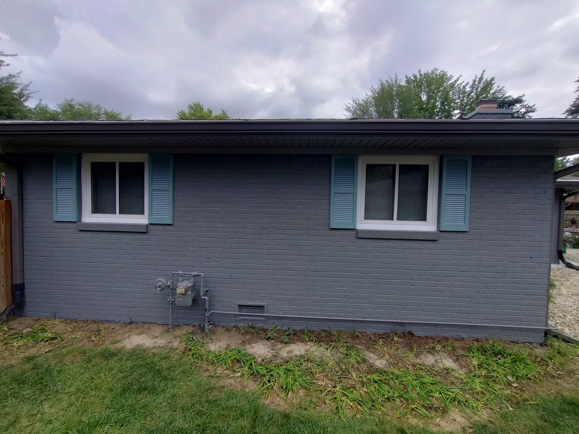A gray brick house with blue shutters and two windows.