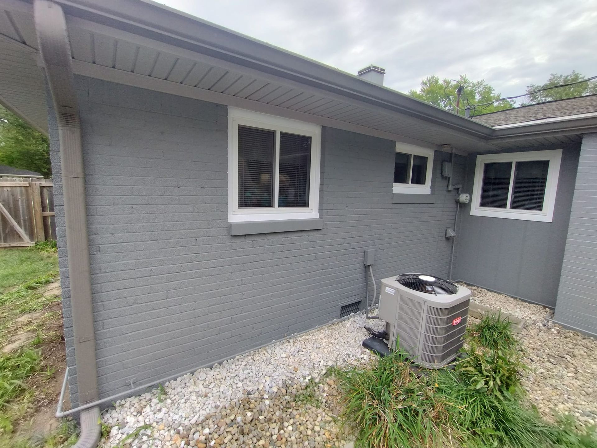 A gray house with a window and air conditioner in the backyard.