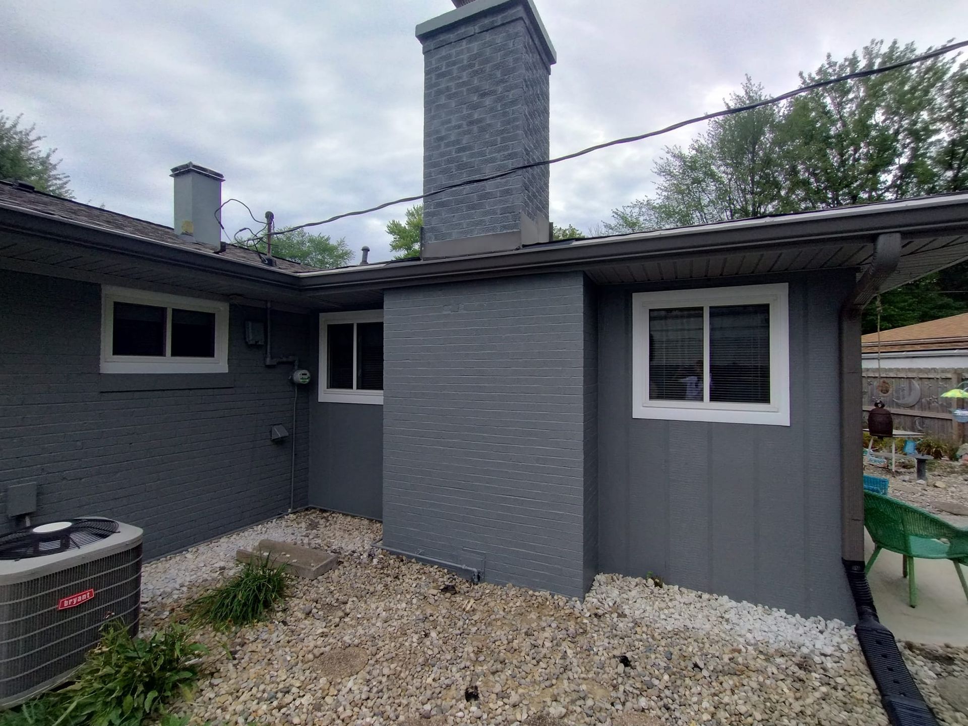 The back of a gray house with a chimney and windows.
