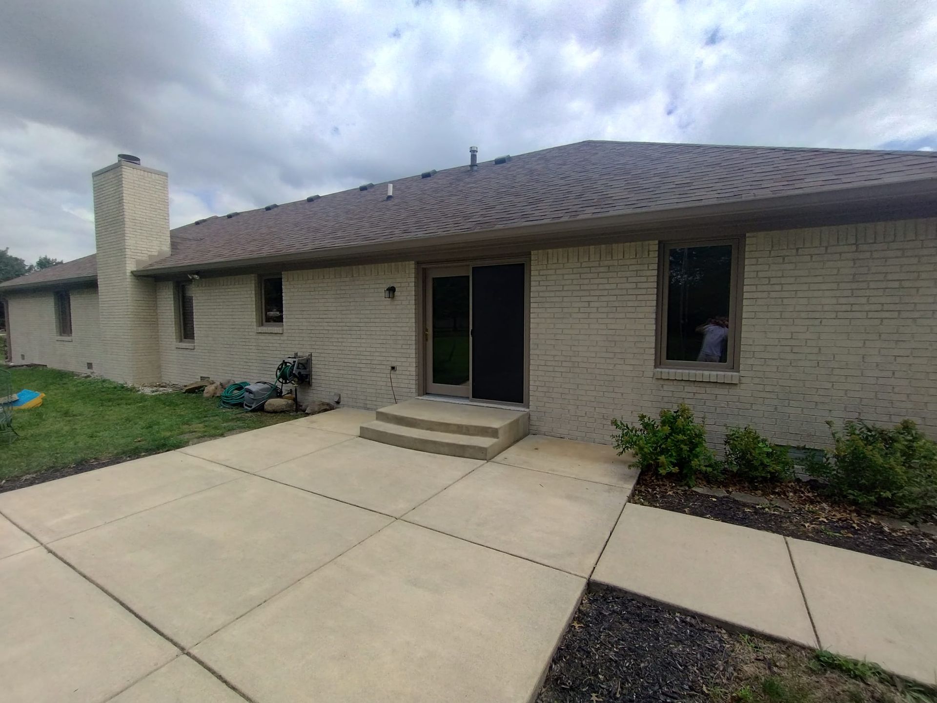 A white brick house with a brown roof and a concrete walkway leading to it.