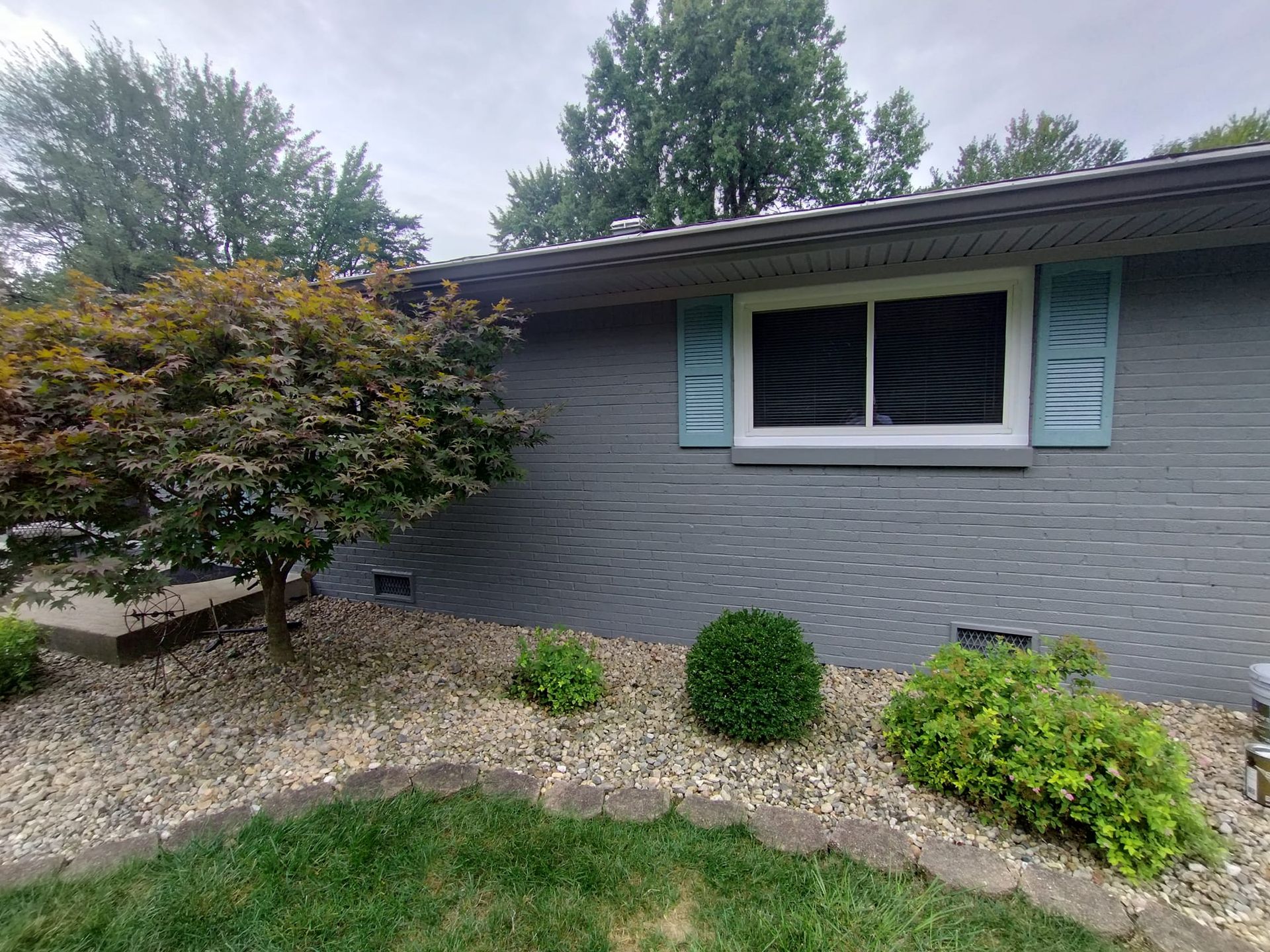 A gray brick house with blue shutters and a large window.
