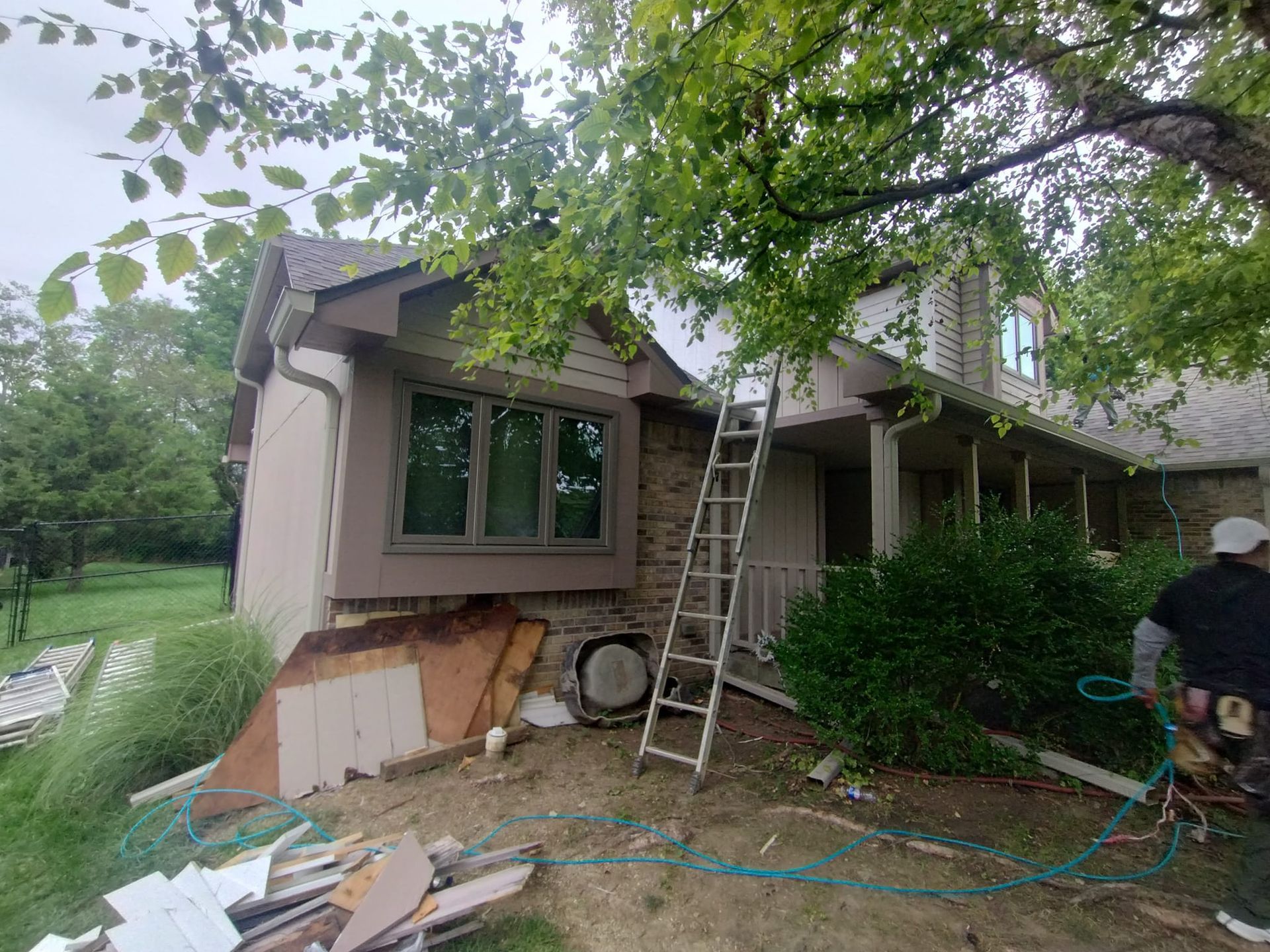 A man is standing in front of a house with a ladder.
