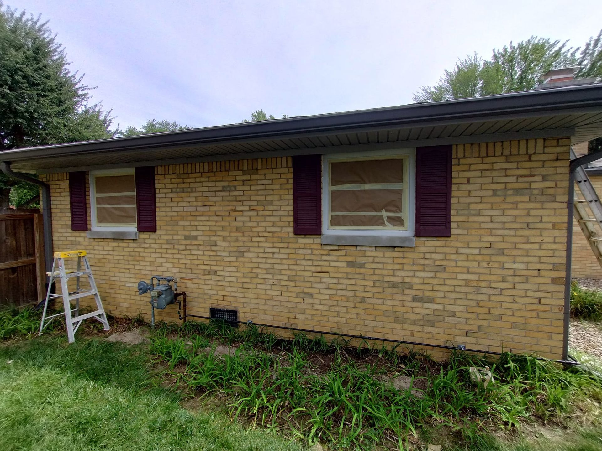 A brick house with purple shutters and a ladder in front of it.