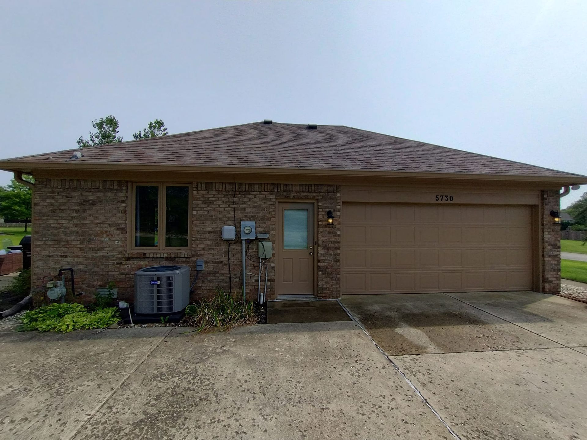 A brick house with a tan garage door and a brown roof.