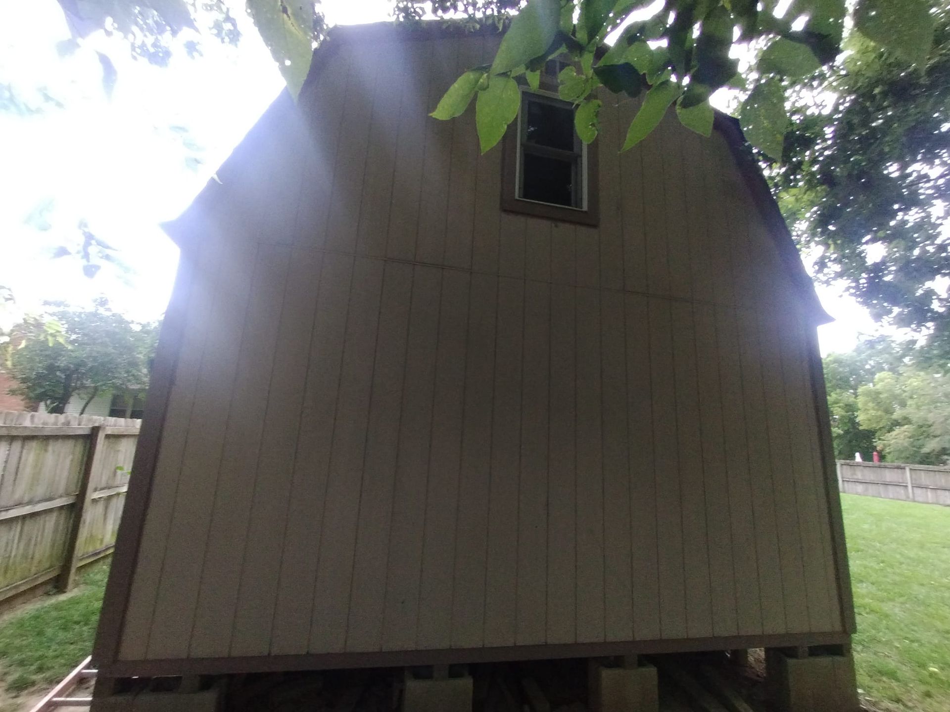 The back of a barn with a window and a fence in the background