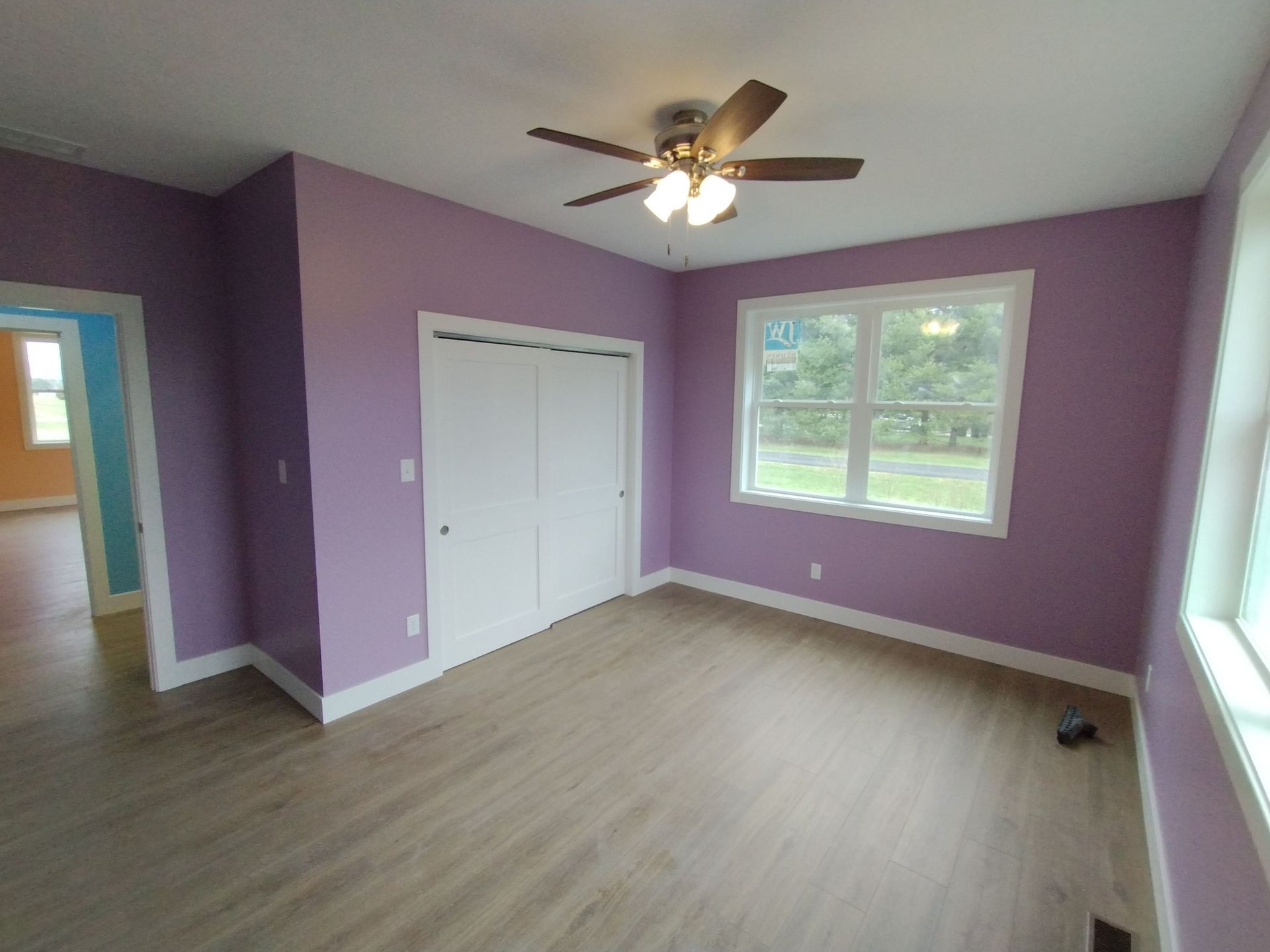 A bedroom with purple walls and a ceiling fan