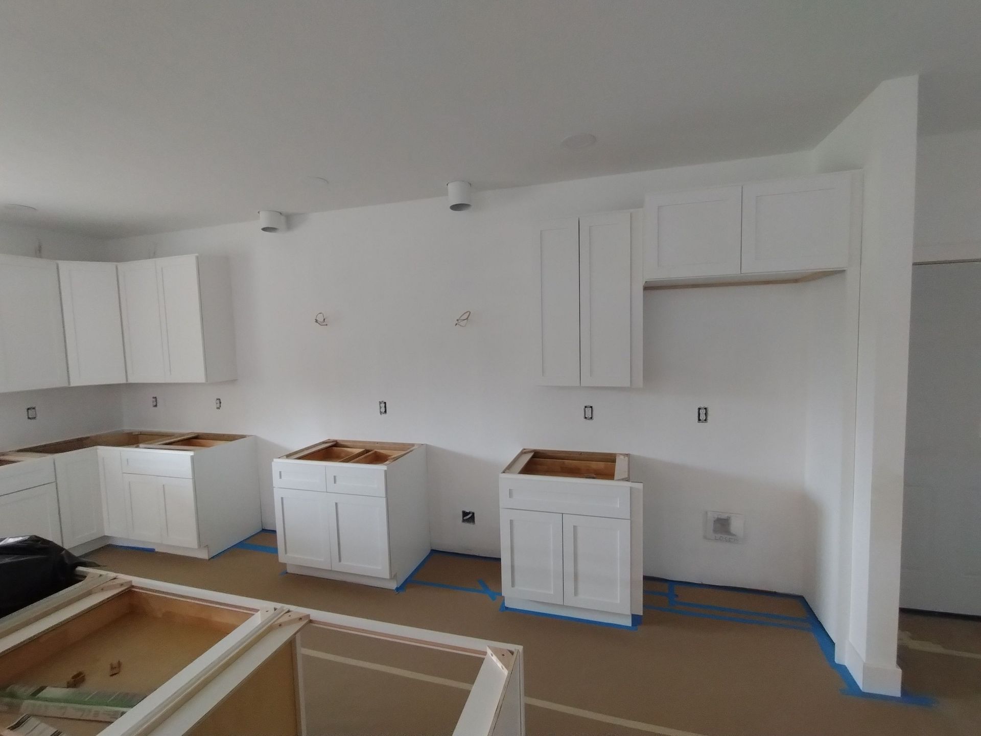 A kitchen under construction with white cabinets and blue tape on the floor.