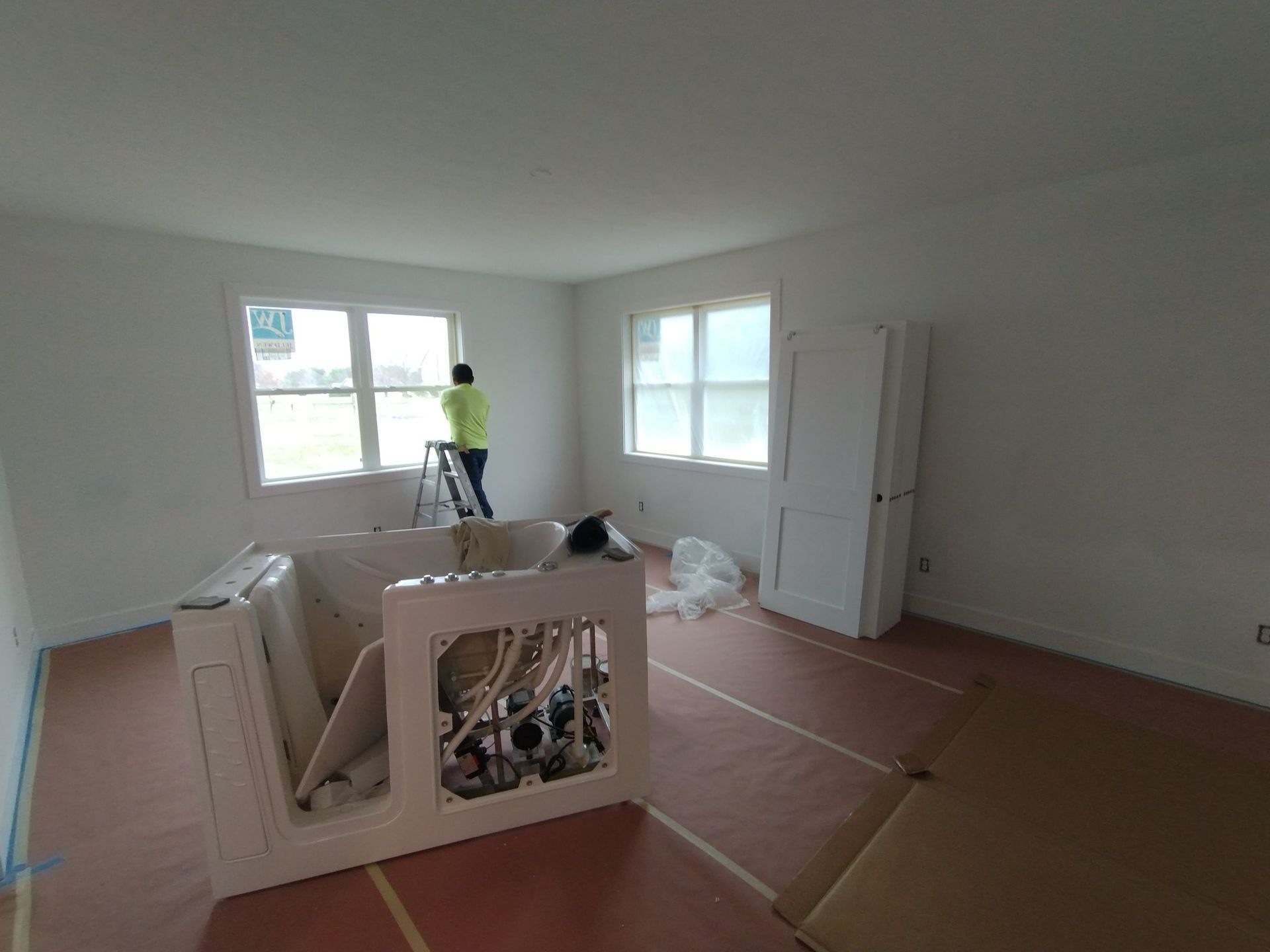 A man is standing on a ladder in a room with a bathtub.