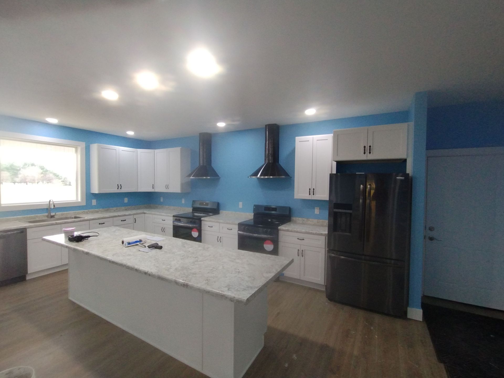 A kitchen with blue walls and white cabinets and a black refrigerator.
