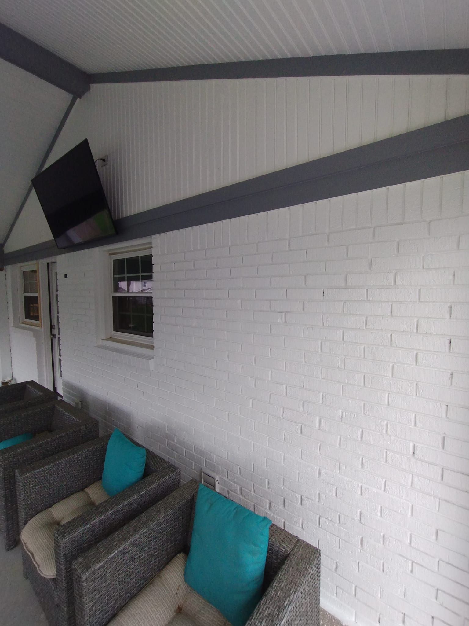 A living room with white brick walls , chairs , and a window.