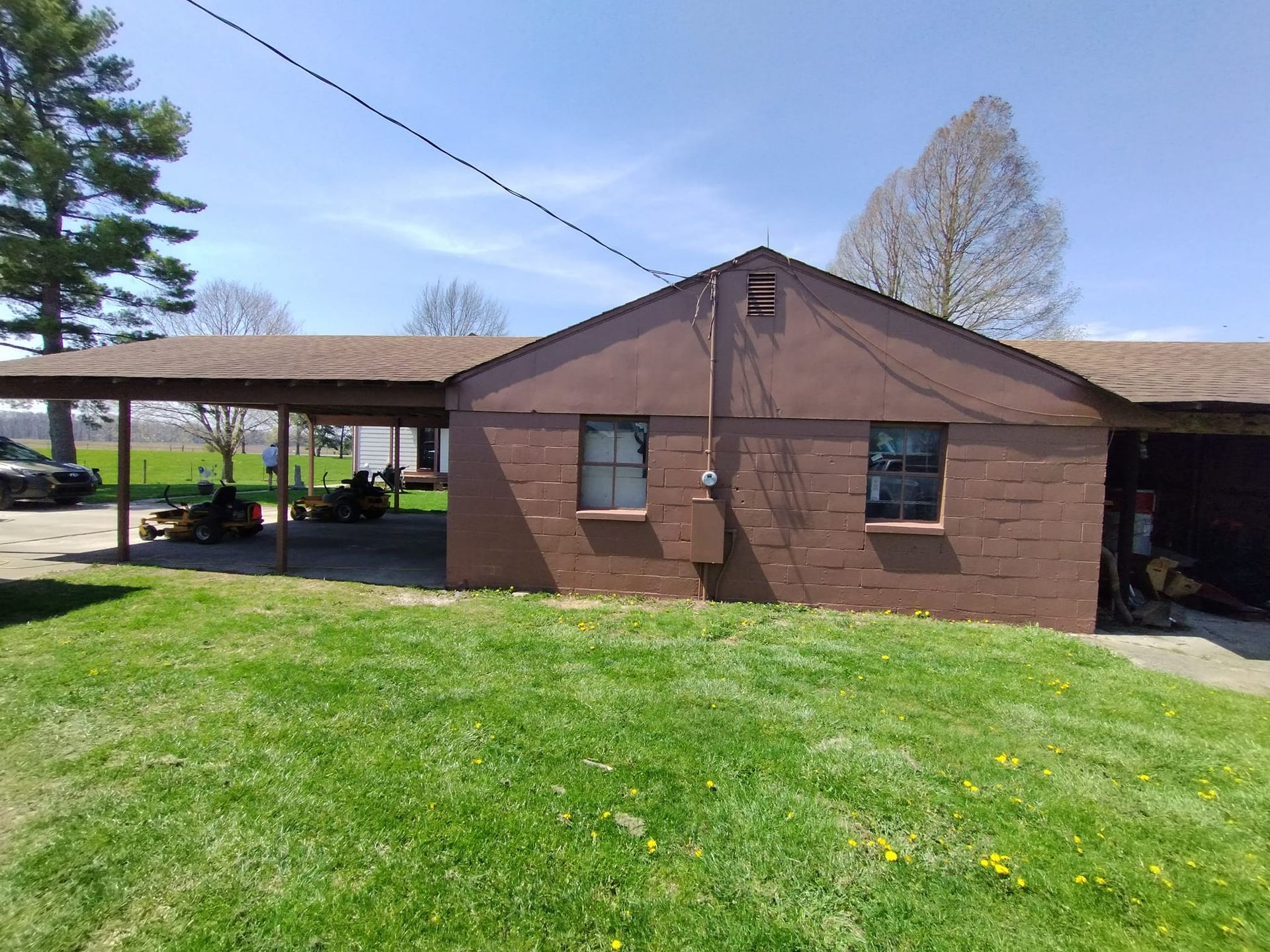 A brown house with a carport and a lot of grass in front of it.
