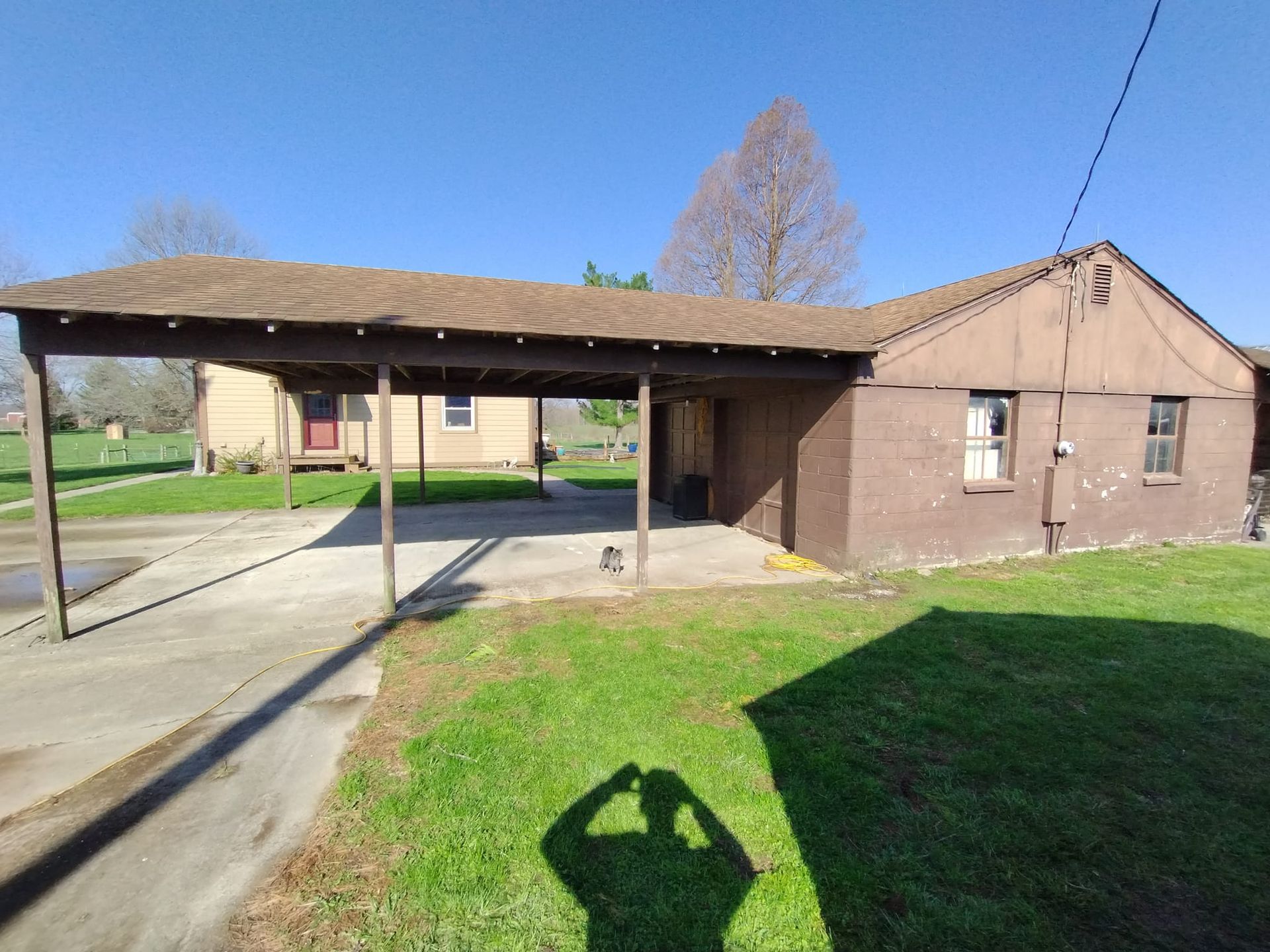 A shadow of a person is cast on the grass in front of a house.