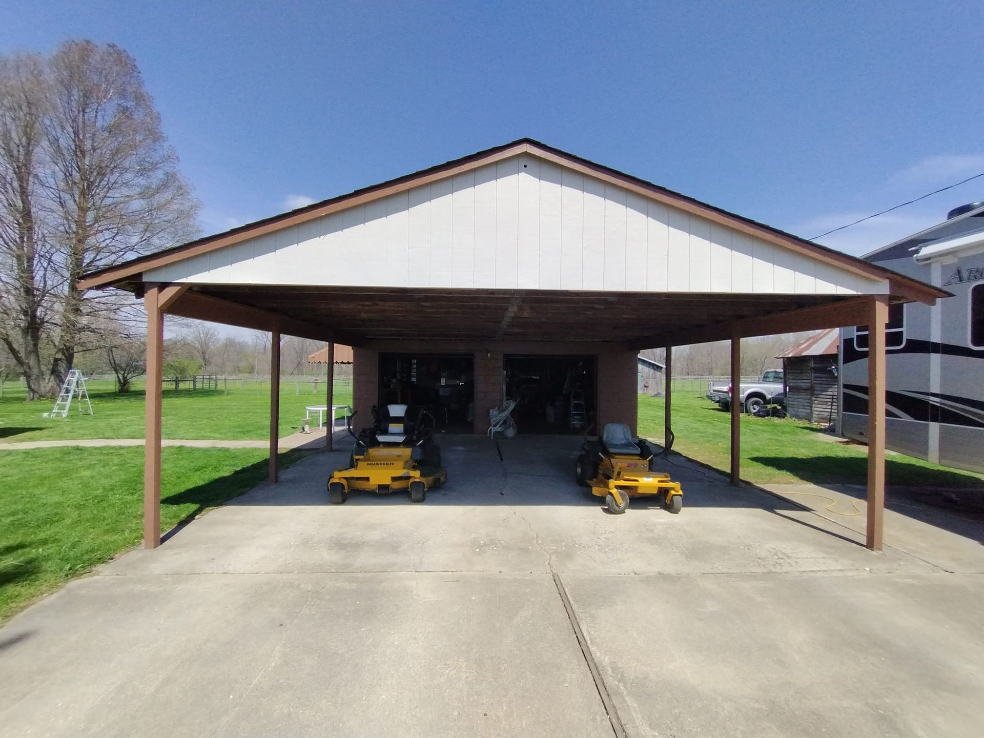 Two yellow lawn mowers are parked under a carport.