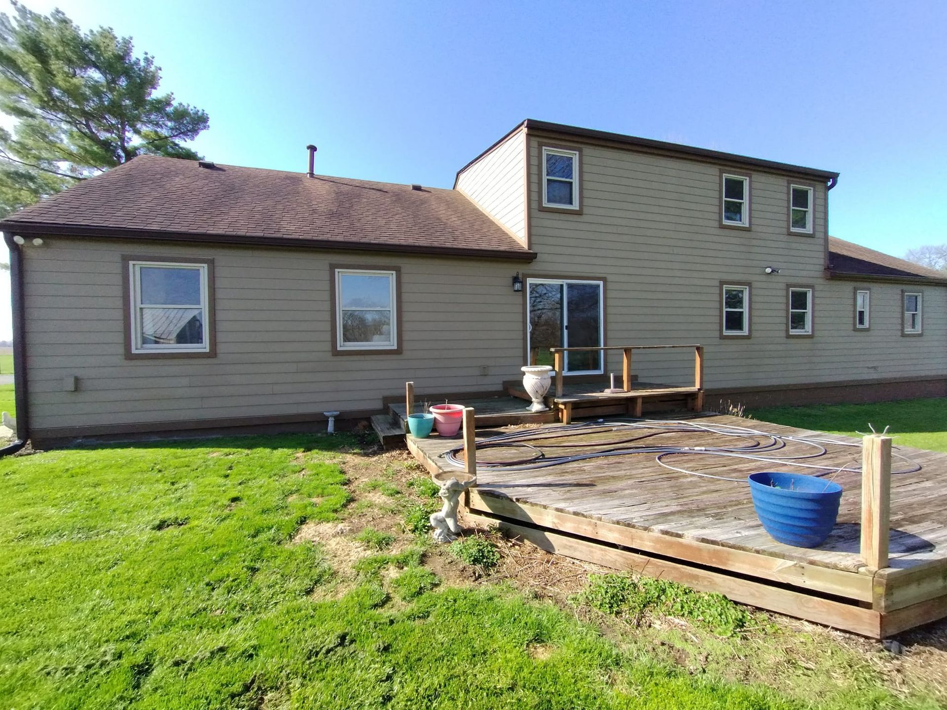 The back of a house with a wooden deck in the grass.
