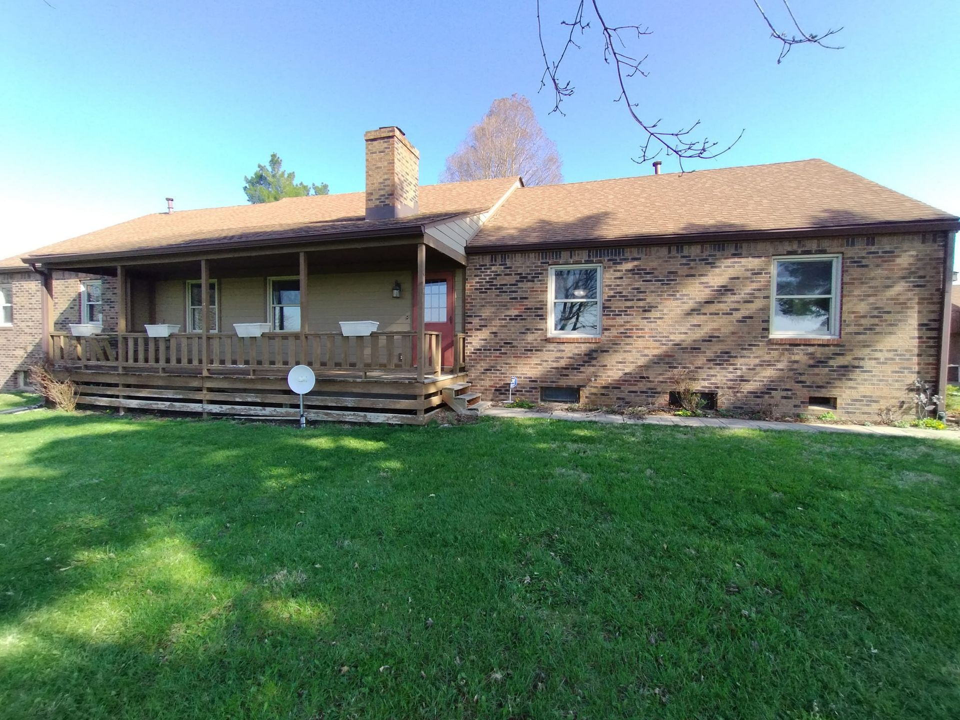 A brick house with a porch and a large lawn in front of it.
