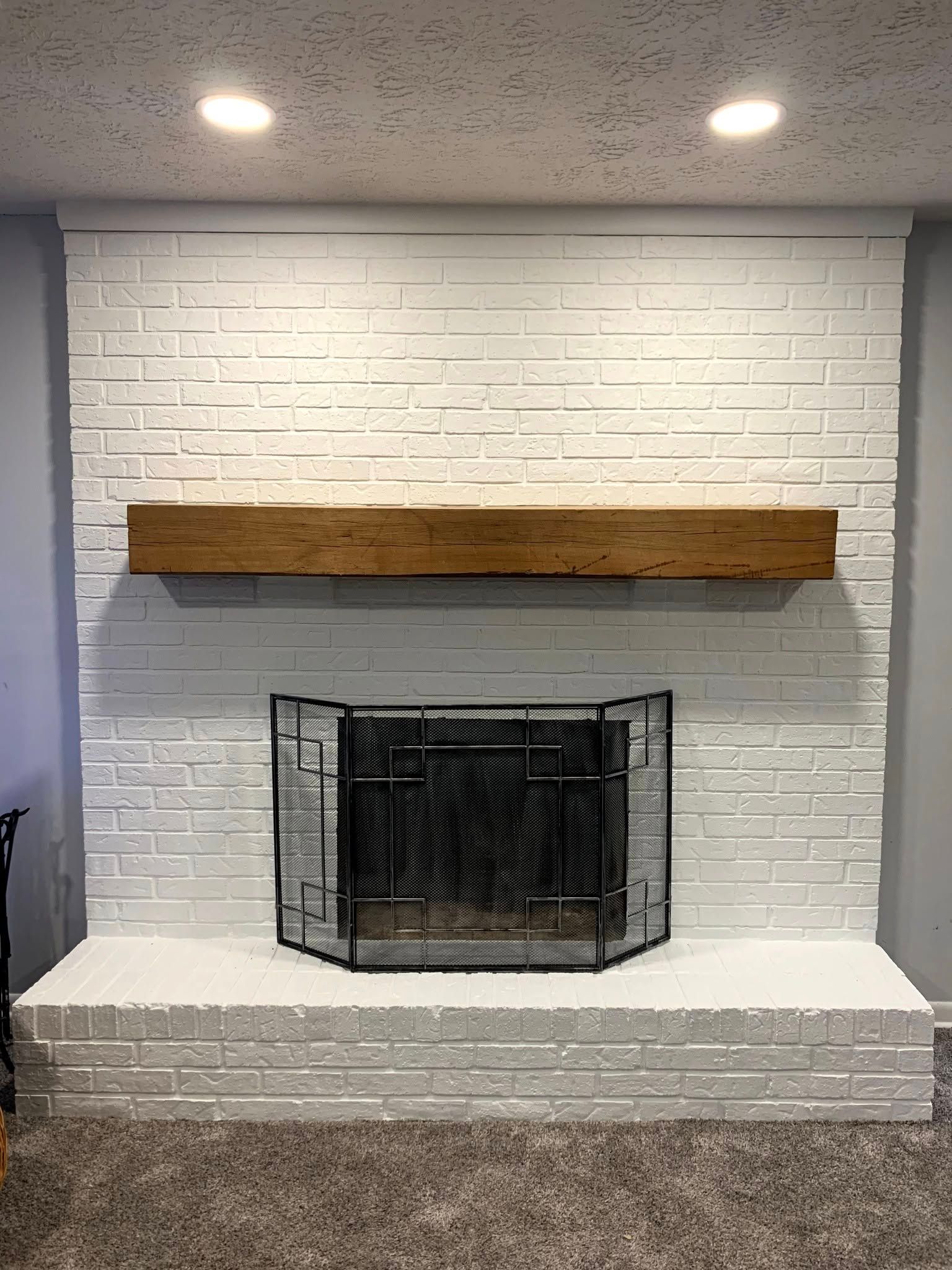 A white brick fireplace with a wooden mantle in a living room.