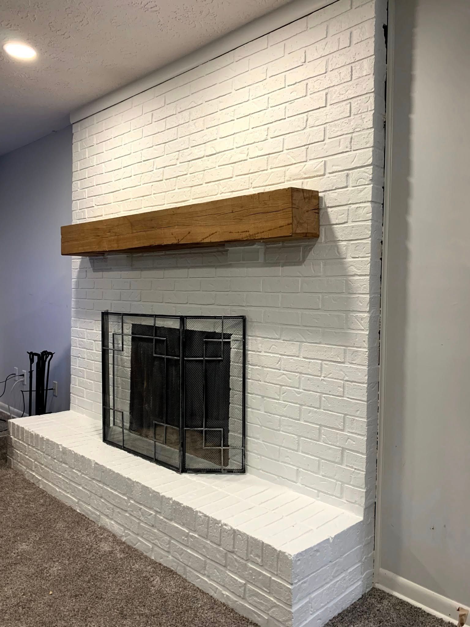 A white brick fireplace with a wooden mantle in a living room.