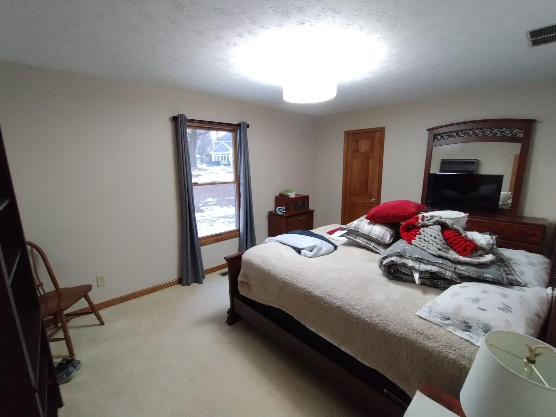 A bedroom with a bed , dresser , mirror and chair.