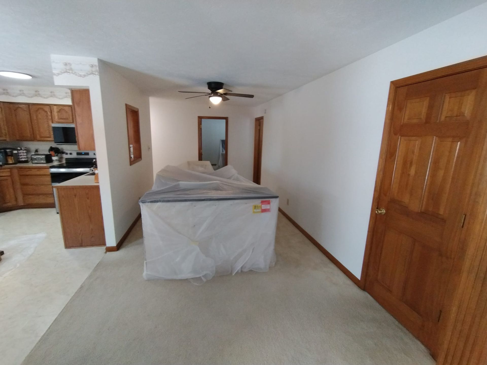 A kitchen with a ceiling fan and a couch covered in plastic