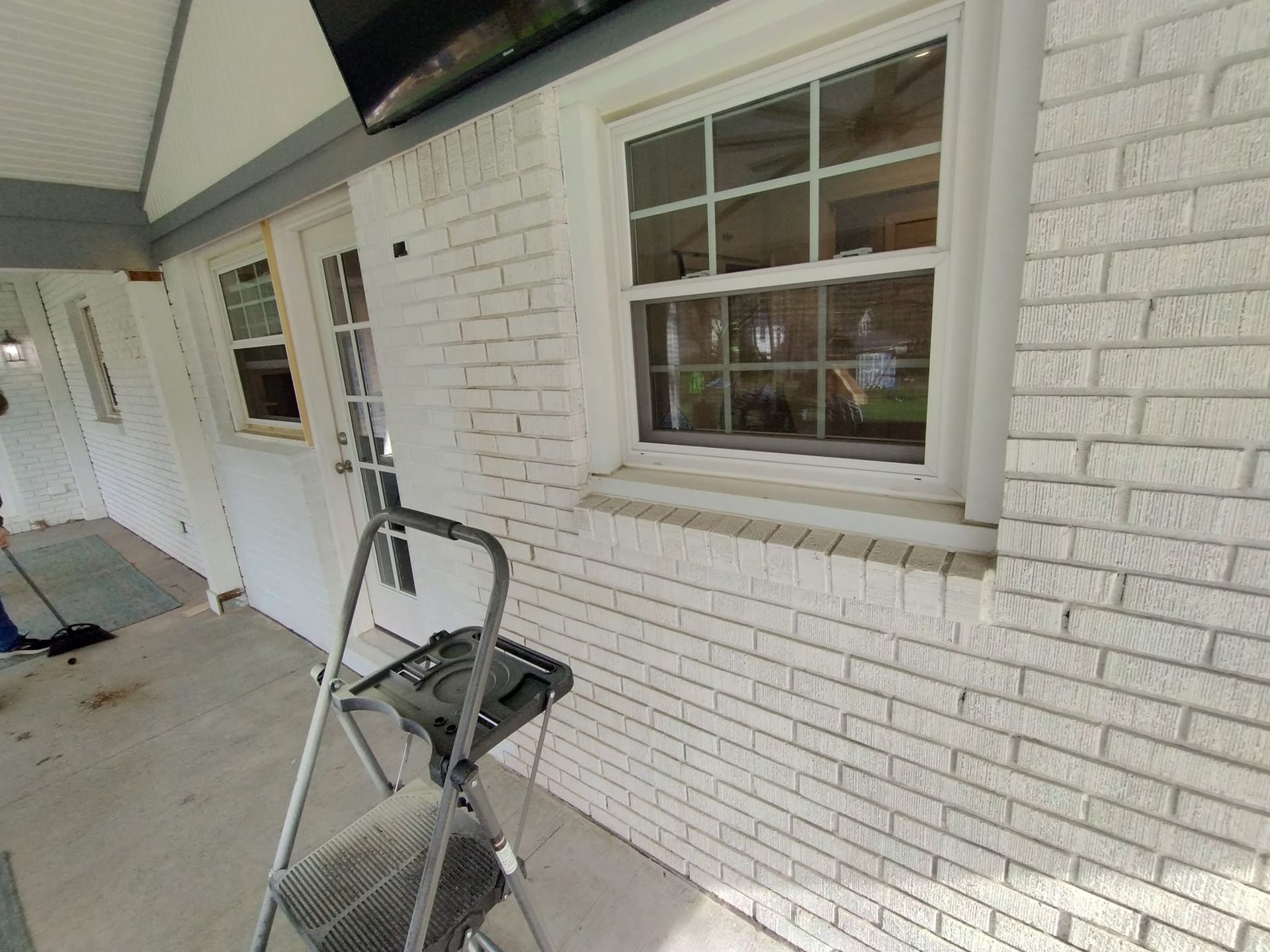 A ladder is sitting on a porch next to a white brick wall.