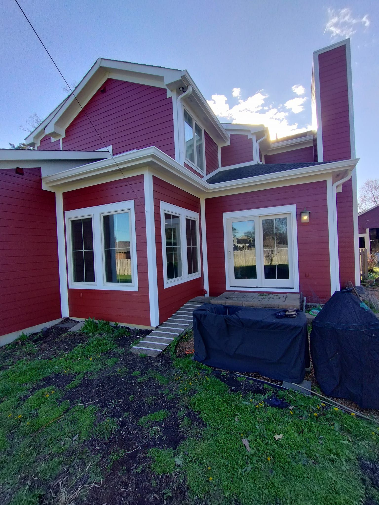 A red house with white trim and windows is sitting on top of a lush green field.