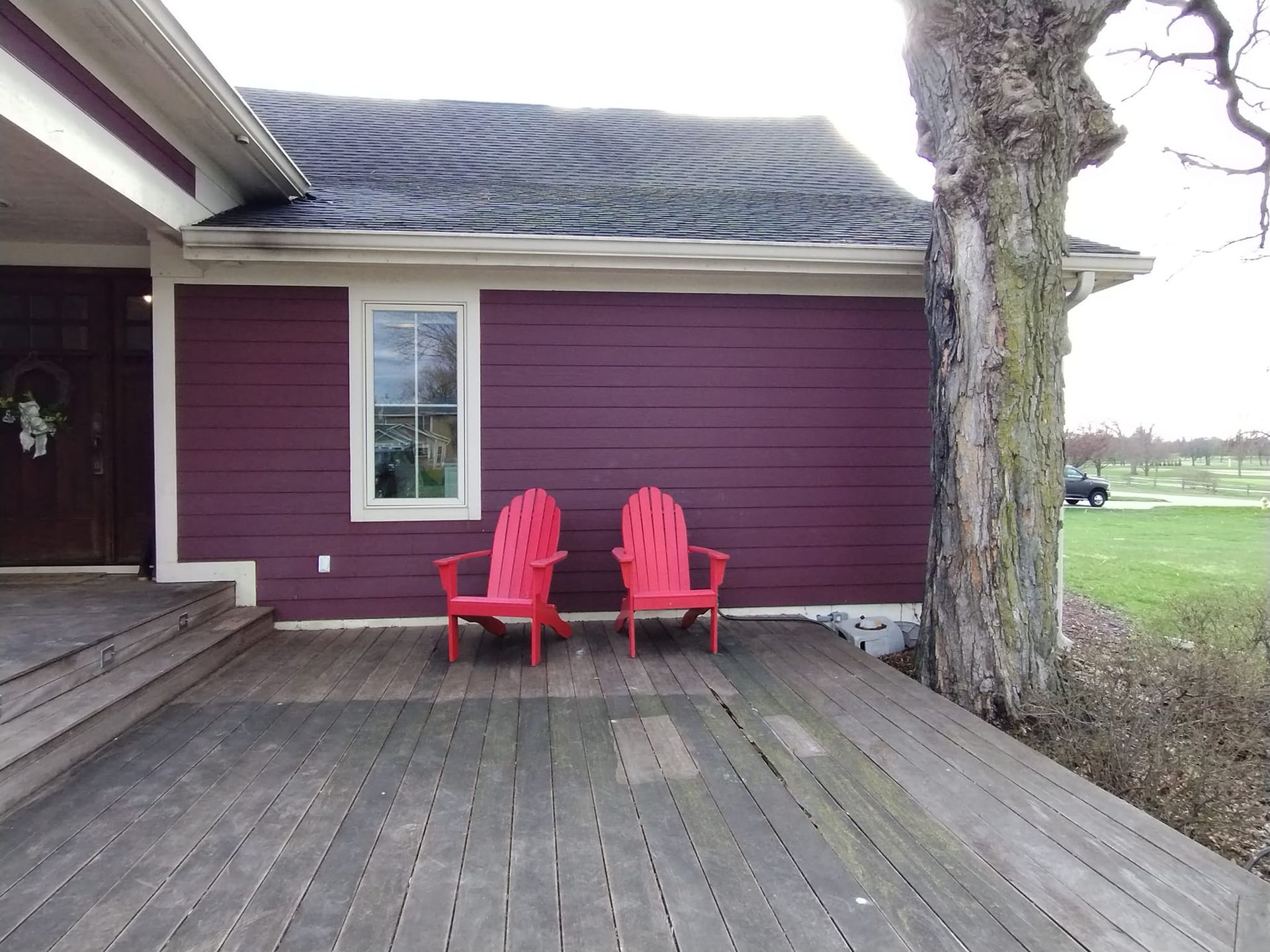 Two red chairs sit on a wooden deck in front of a purple house