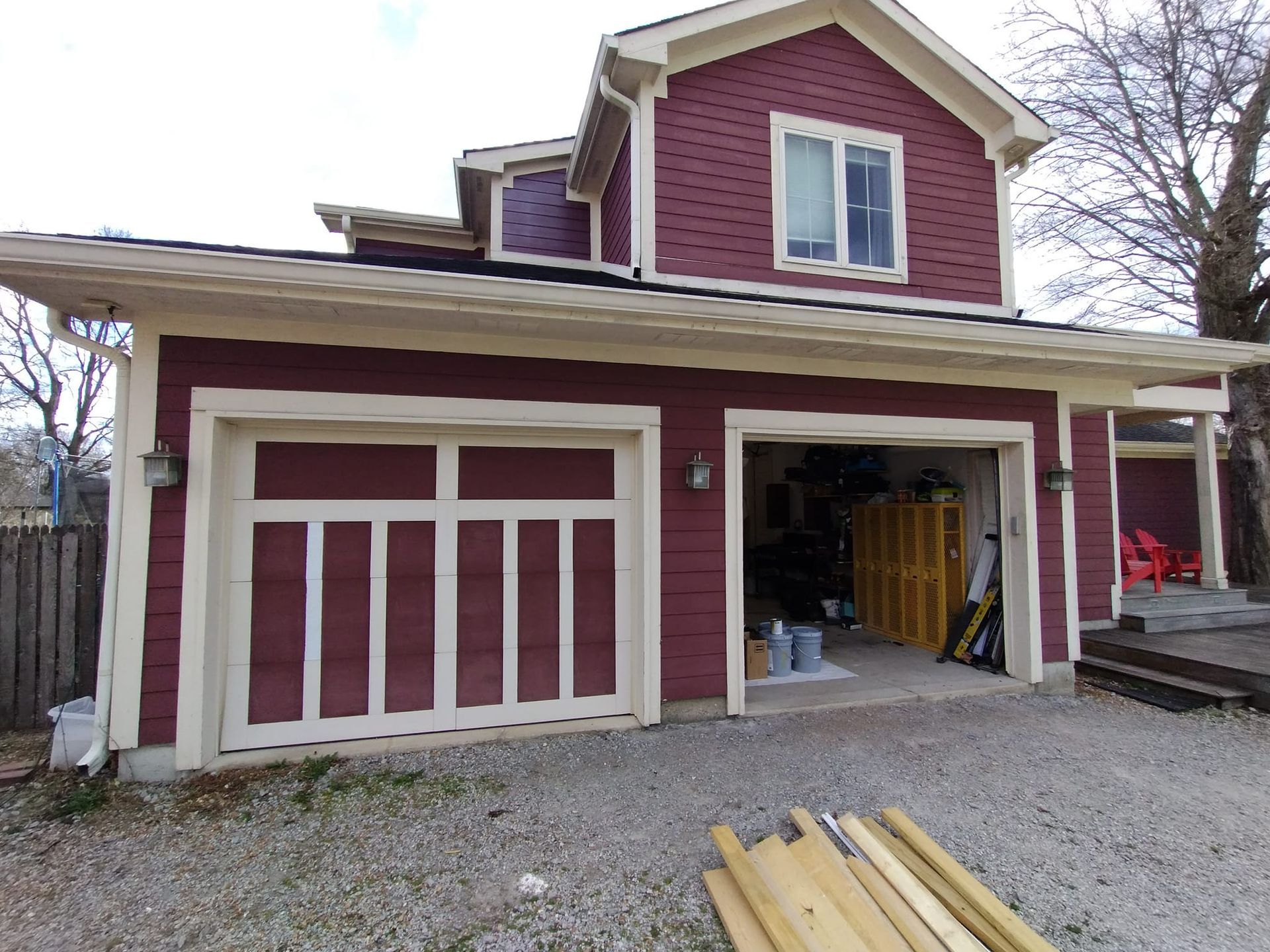A red house with a garage and a stack of wood in front of it.