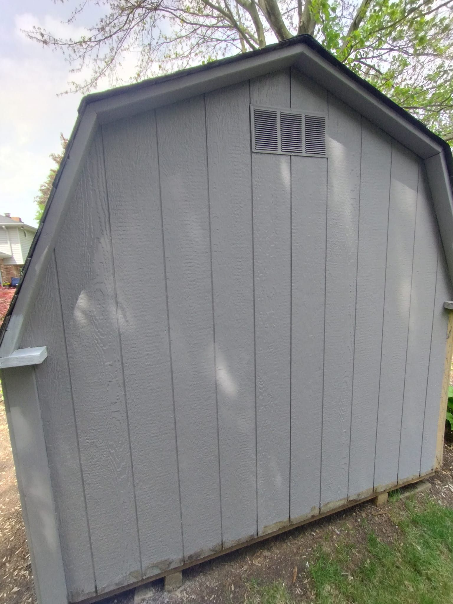 A gray shed with a black roof is sitting in the grass.