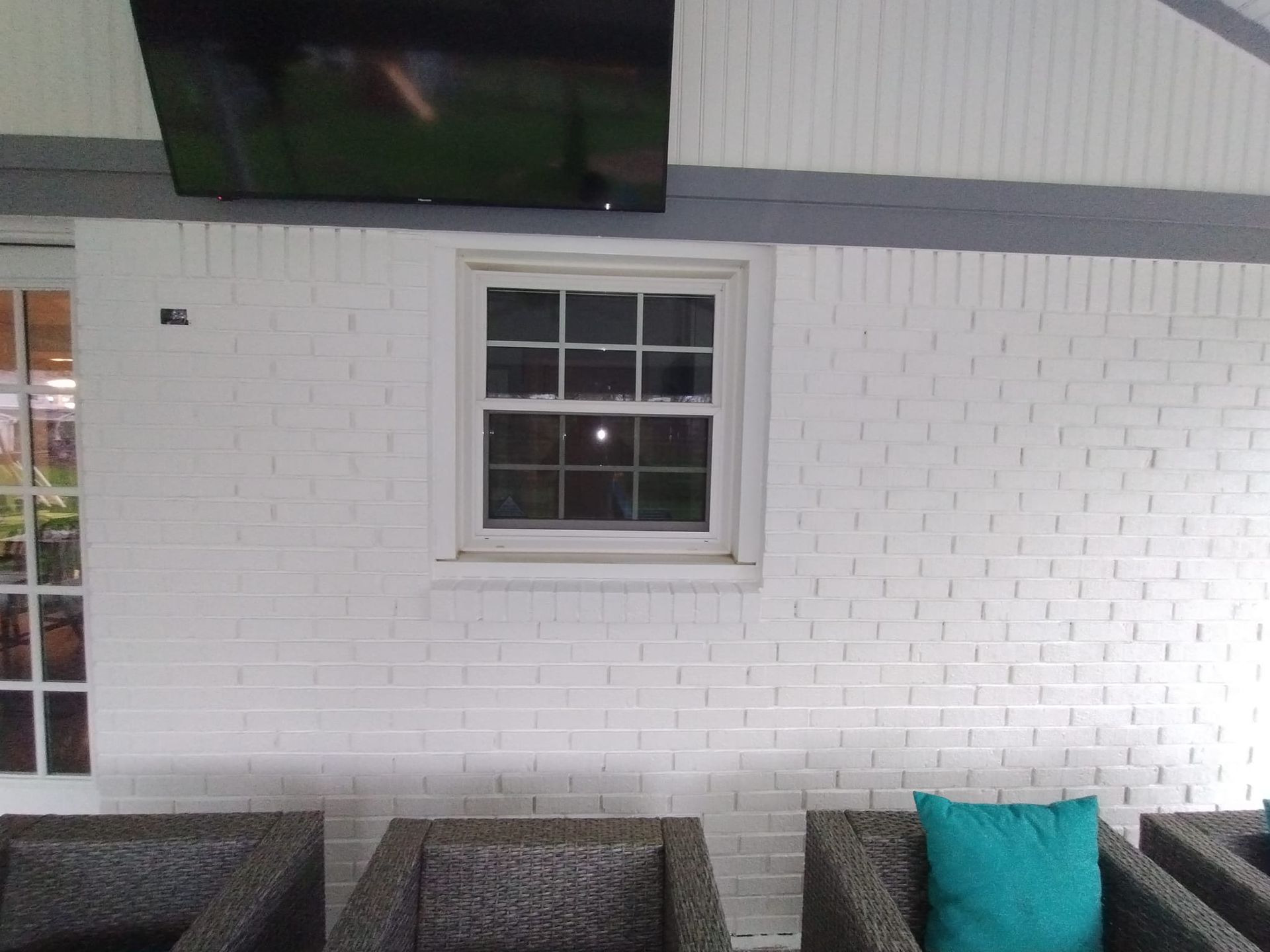 A white brick wall with a window and a flat screen tv above it.