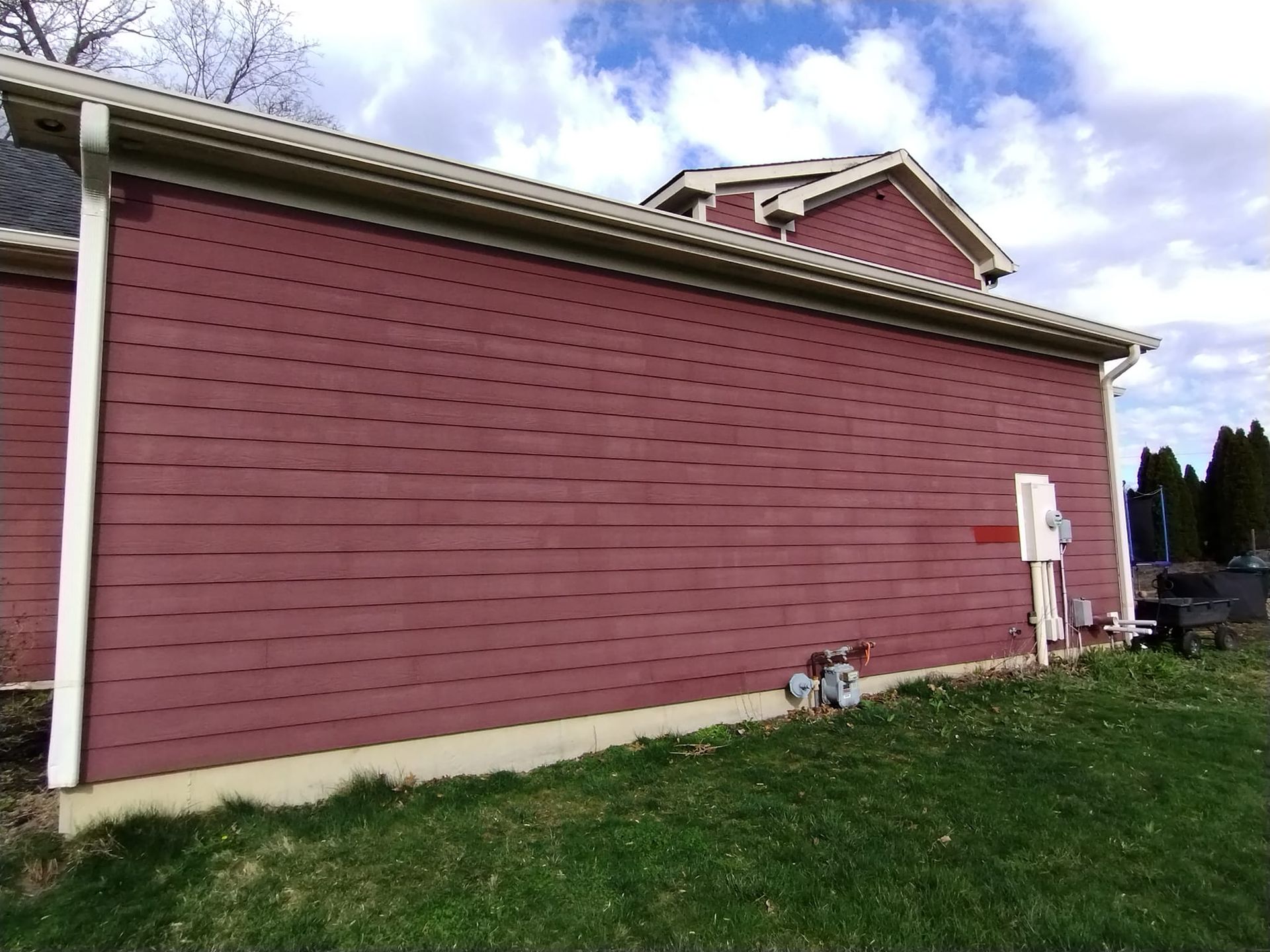 A red house with a white gutter is sitting on top of a lush green field.