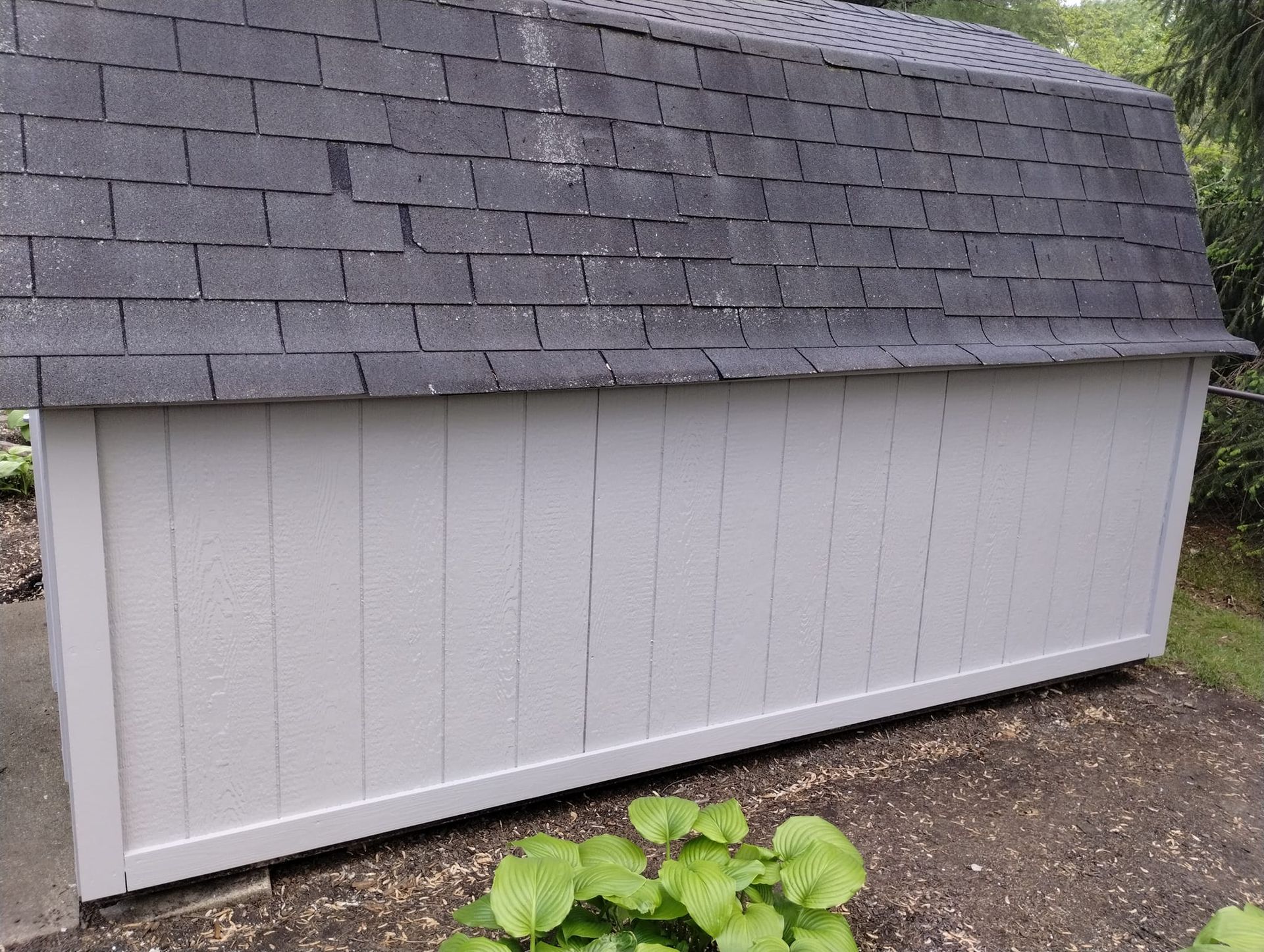 A white shed with a black roof is sitting in the dirt