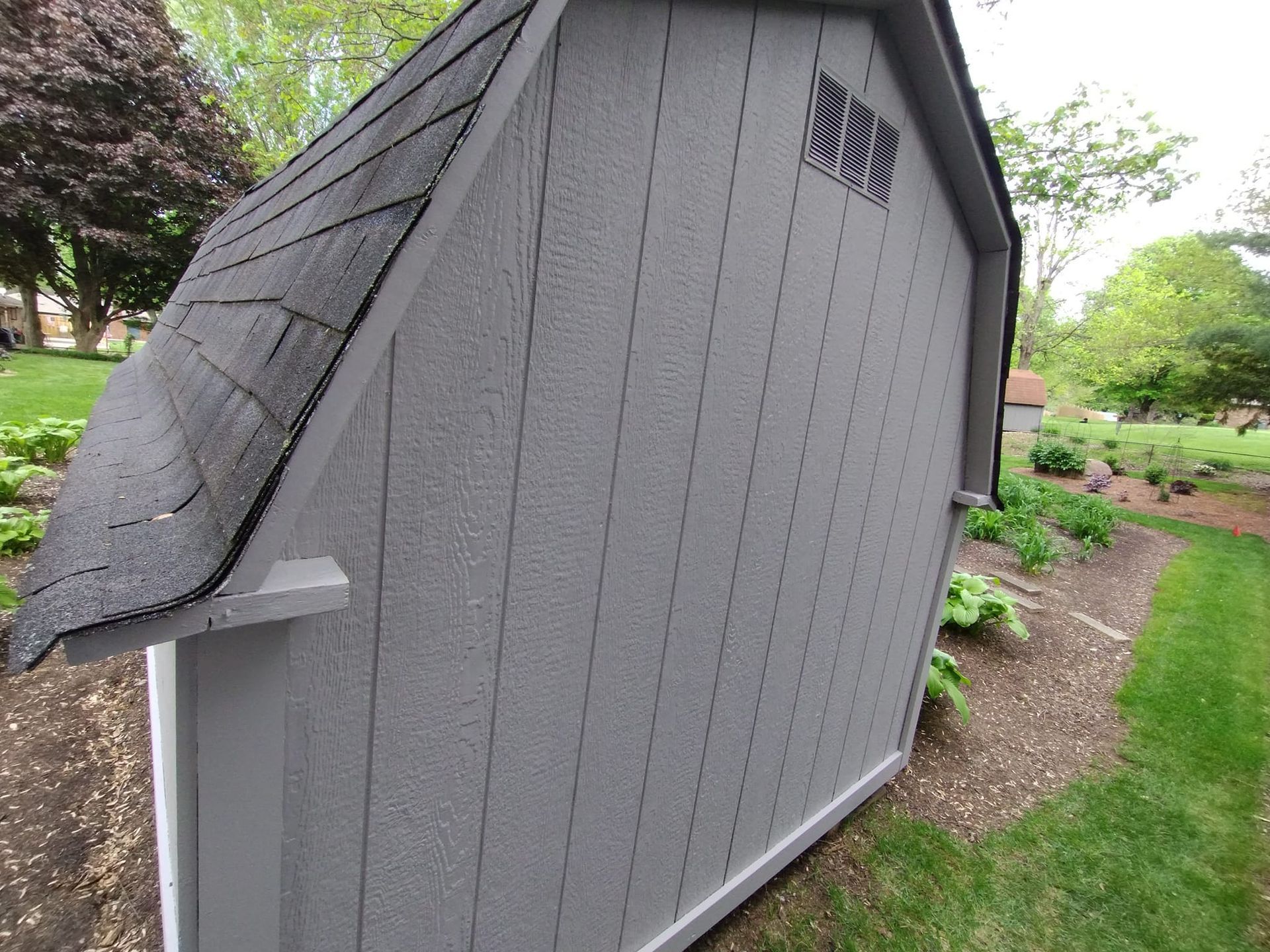 A gray shed with a black roof is sitting in the grass.